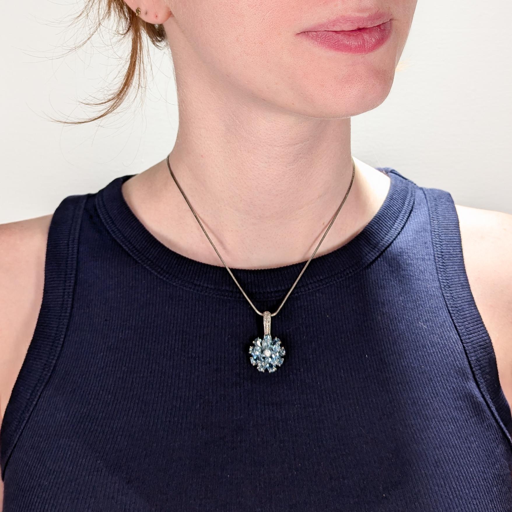 A fine stylized flower pendant.

In 14k white gold.

Comprising 14 oval cut prong set blue tourmaline gemstones set as petals surrounding a prong set round cut diamond center. 

Supported by an integral jump ring pave set with single cut white