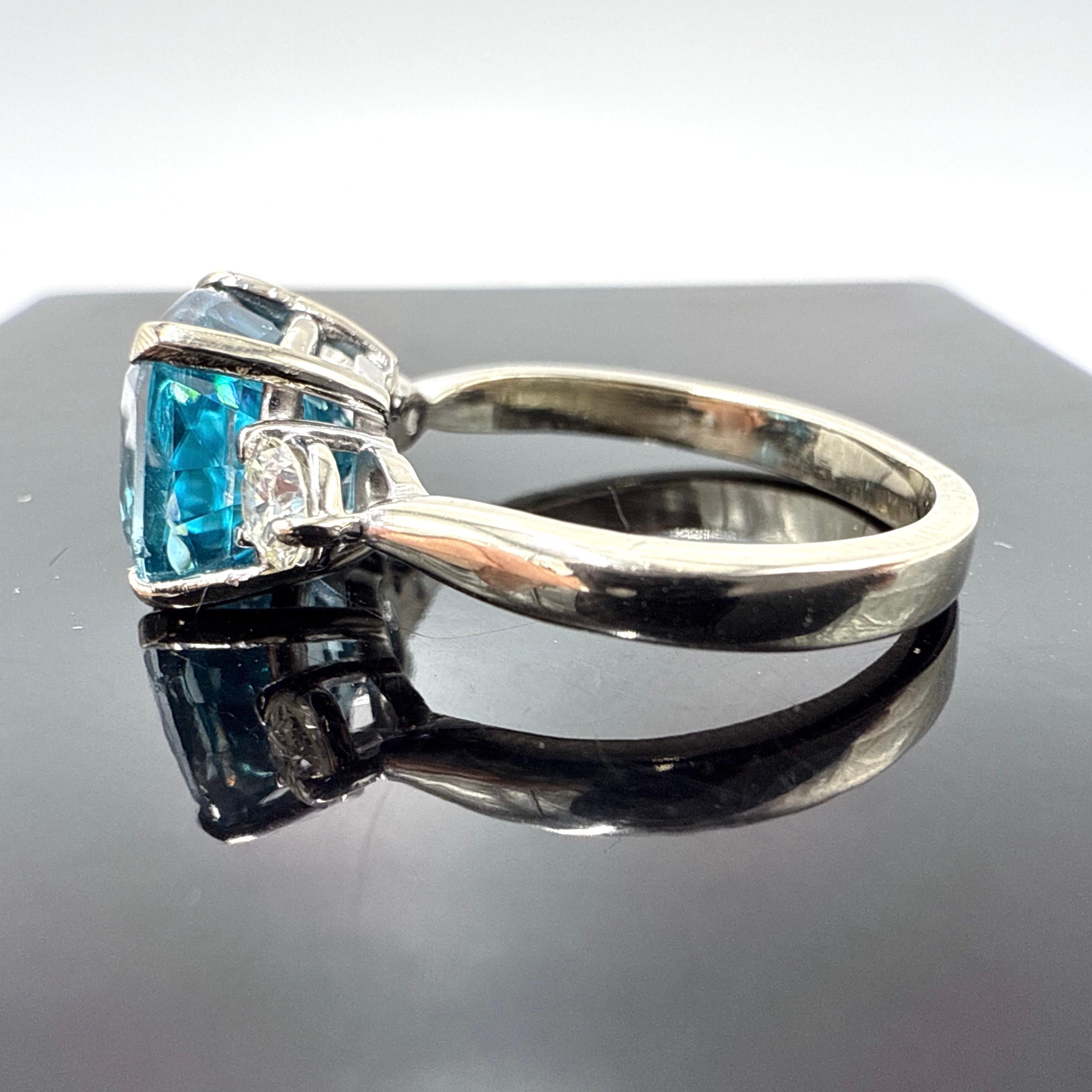 Questo anello in oro bianco 14K presenta un sorprendente zircone blu sfaccettato a cuscino da 4,24 carati, incastonato in una doppia galleria a quattro griffe. Lo zircone misura circa 8,15 mm x 8,15 mm x 6,30 mm e presenta una tonalità di blu medio