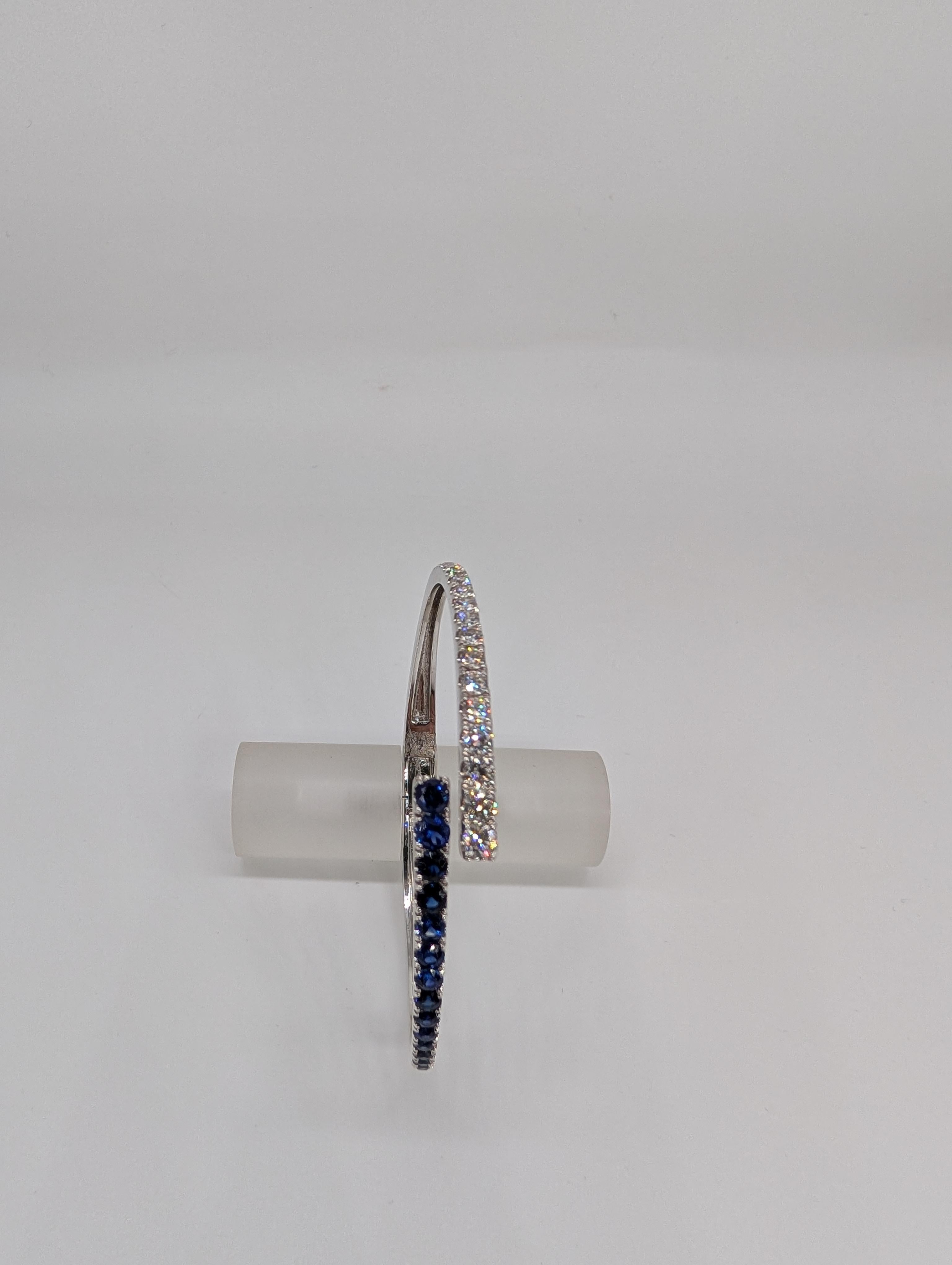 This 14-karat white gold bypass bangle is a stunning display of refined luxury and modern design. Featuring a graceful arrangement of graduated diamonds and sapphires, the piece showcases the diamonds (1.44ct) and sapphires (1.85ct) in an elegant,
