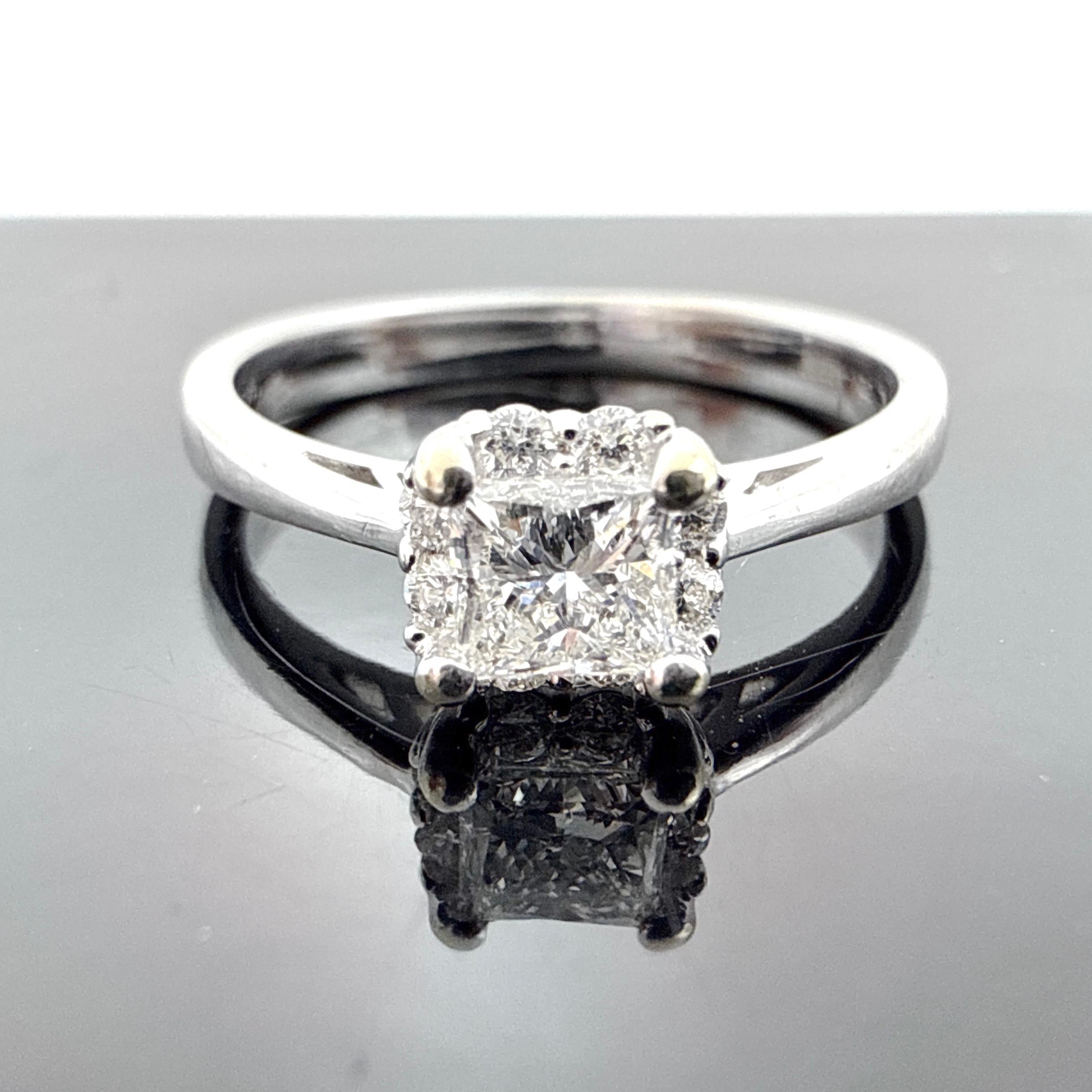 Questo anello di fidanzamento è realizzato in oro bianco 14K, fuso in cera, assemblato e rifinito a mano. Presenta un diamante centrale quadrato incastonato in una montatura a quattro griffe, circondato da pietre d'accento incastonate. La fascia