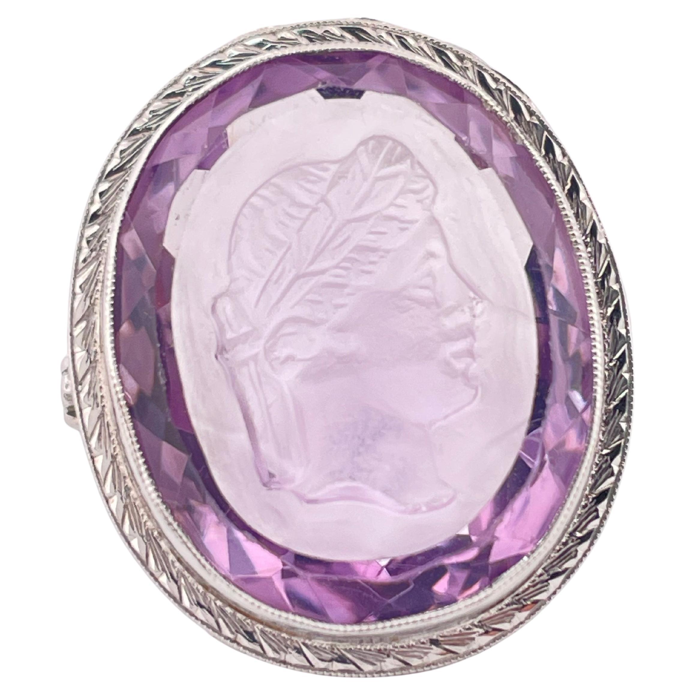 Cette exquise bague en or blanc 14k présente une intaille d'améthyste sculptée de main de maître, avec le profil classique d'une figure couronnée de laurier rappelant l'art romain antique. L'améthyste de taille ovale, avec sa riche teinte lavande et