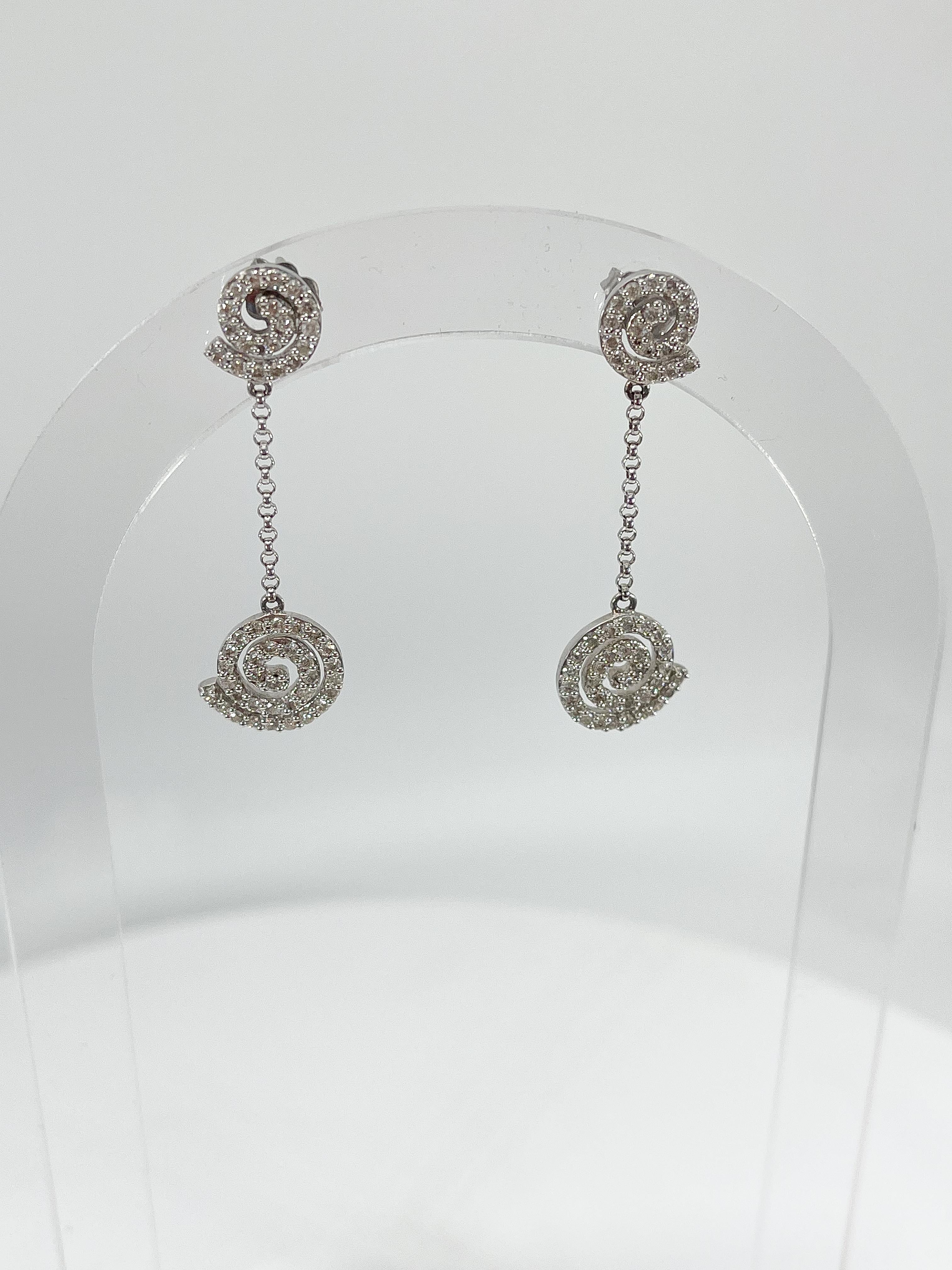 14k white gold circle swirl 1.06 CTW diamond drop earrings. The diamonds in these earrings are all round, they have a width of 11.7, a length of 40 mm, and they have a total weight of 4.2 grams.