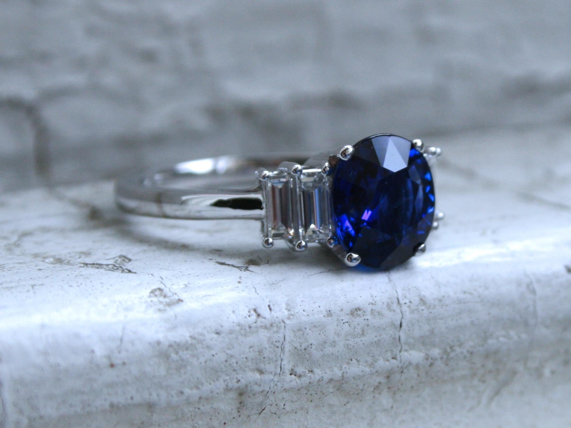 This Beautiful Diamond and Sapphire Ring is a stunning, unique design! Crafted in 14K White Gold, the design features a classic five stone layout, with an Oval Sapphire center, and unique Baguette Cut Diamonds set North South on the side. So