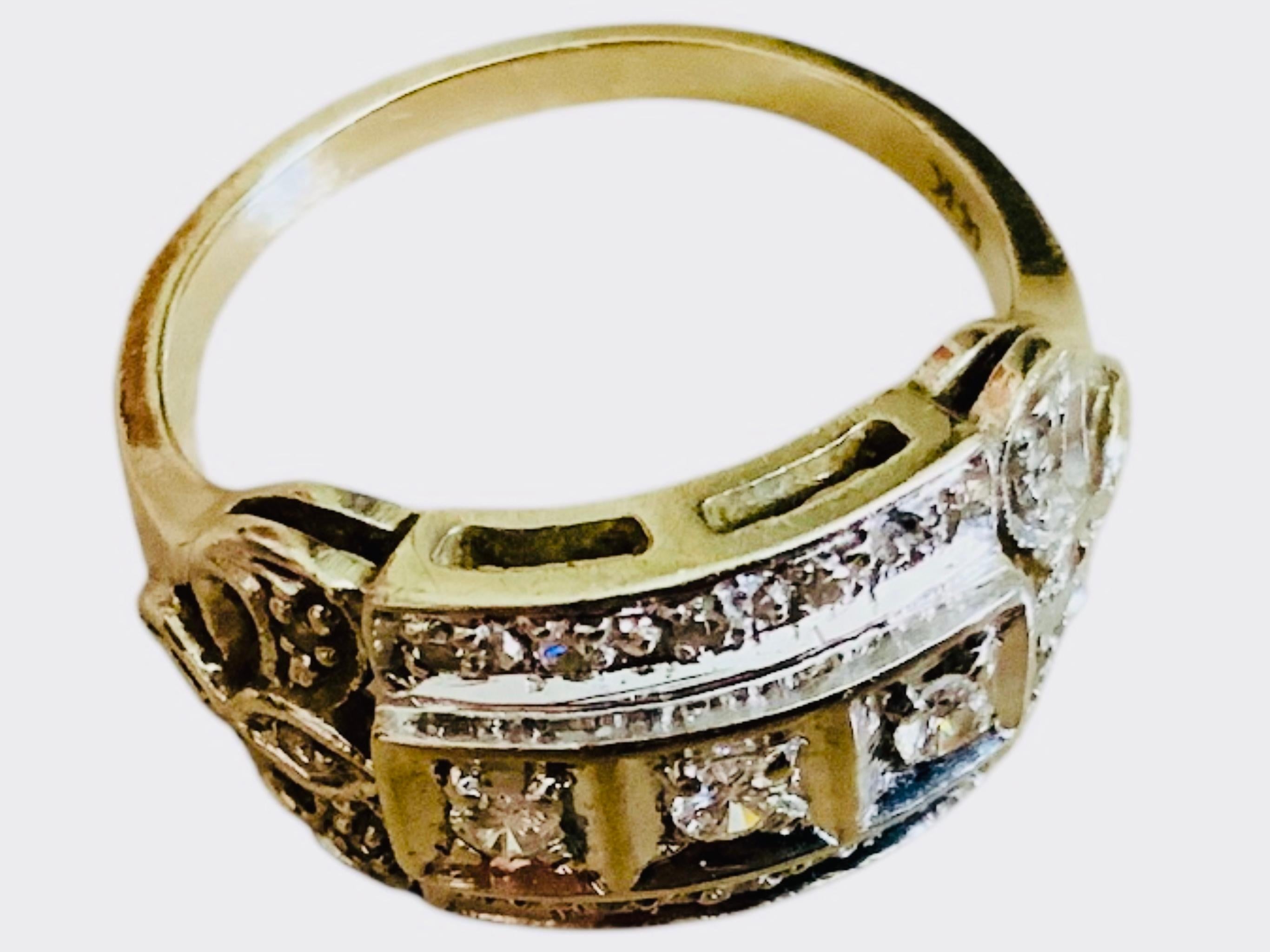 This is a 14 K White Gold Diamond Art Deco Ring. It depicts a wide white gold band adorned by three rows. The middle one is made of three round brilliant diamonds in pave setting in a square shaped frame. The rows below and above the middle one are