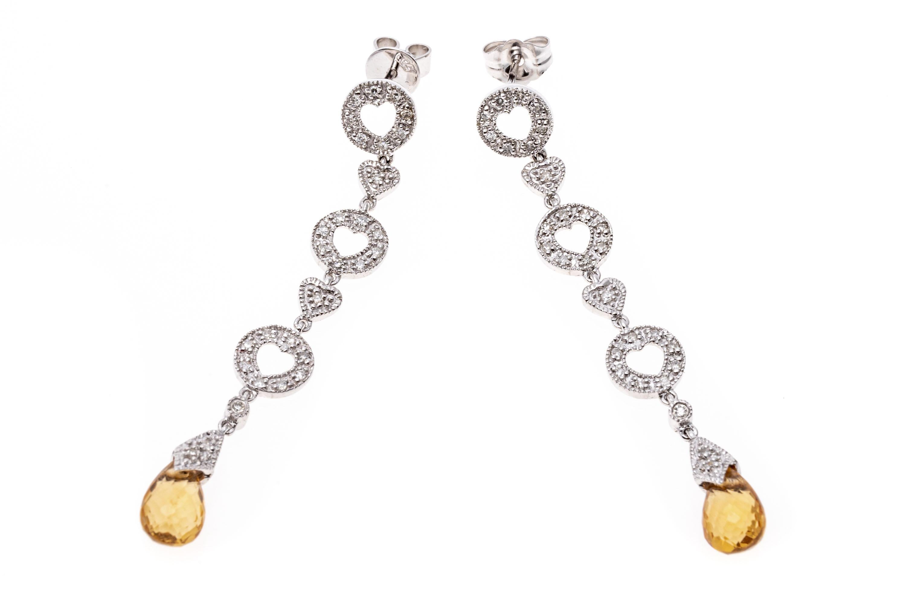 14k white gold earrings. These whimsical pendant earrings have a pretty heart motif top and stacked heart line, set with round faceted diamonds. Suspended from the line is a drop with a faceted briolette shaped, light yellow citrine stones. The