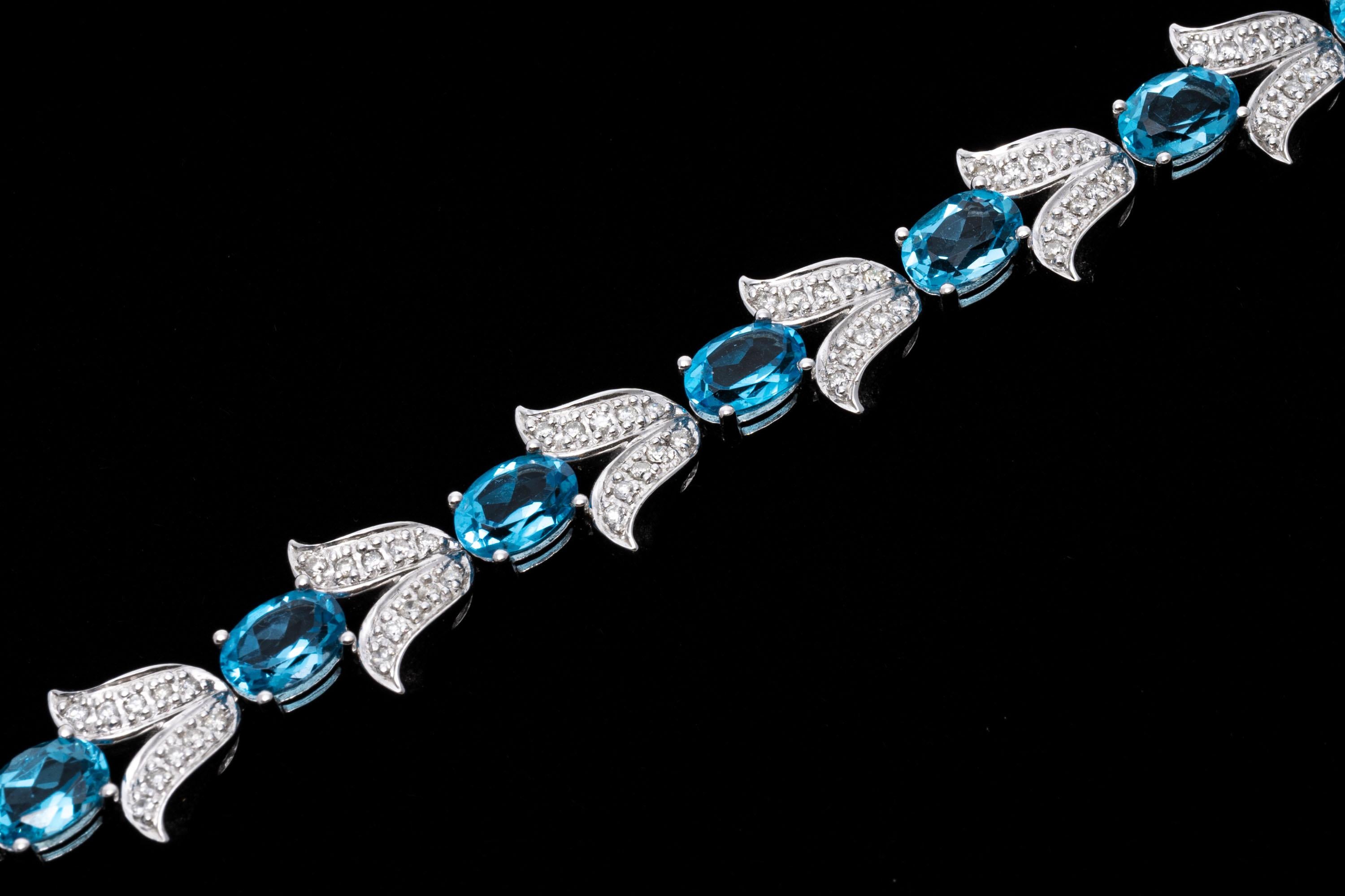 14k white gold bracelet. This beautiful bracelet features oval faceted, medium blue color blue topaz stones, approximately 10.45 TCW, prong set, alternating with tulip shaped links set with accent diamonds, 1.10 TCW. The bracelet has a hidden box
