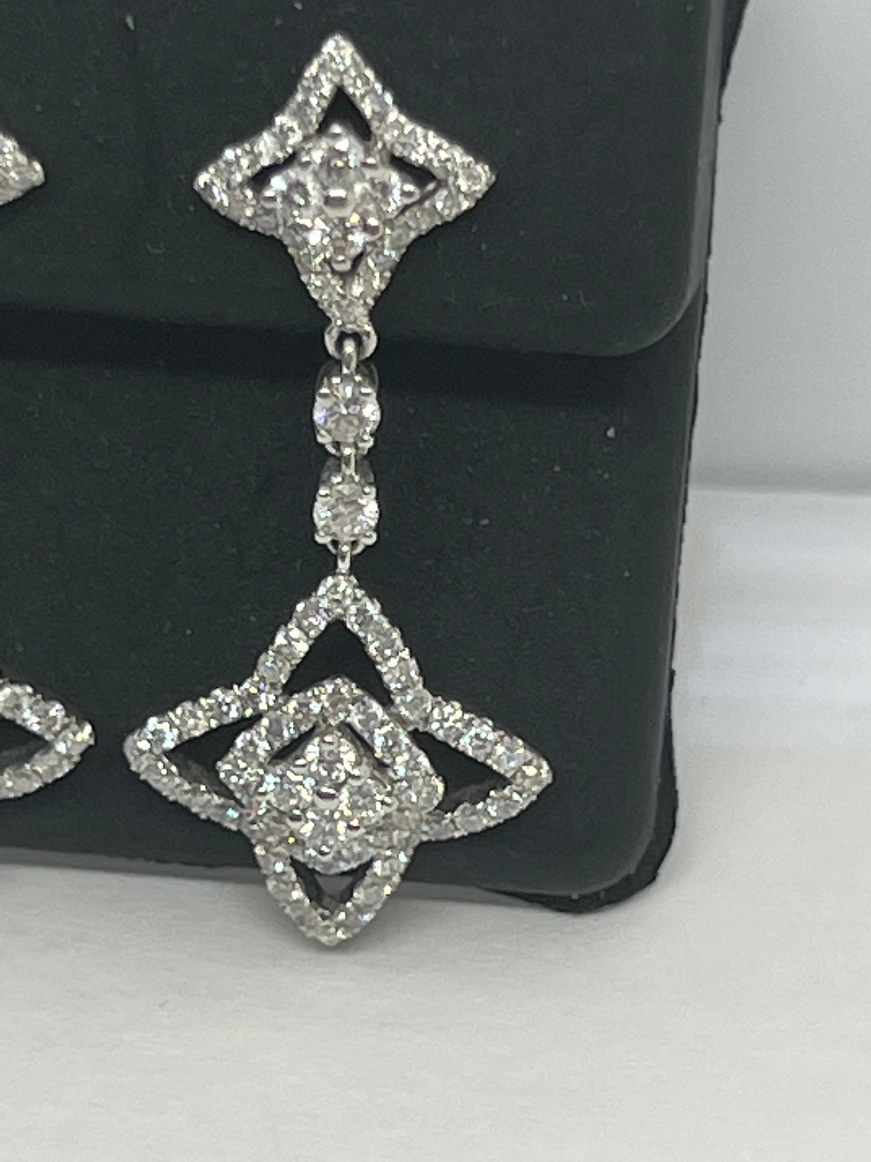 Add a touch of sparkle to your outfit with these stunning 14k white gold dangle drop earrings. The star-shaped design is adorned with natural round white diamonds that glisten in the light, making them perfect for any special occasion. The pavé