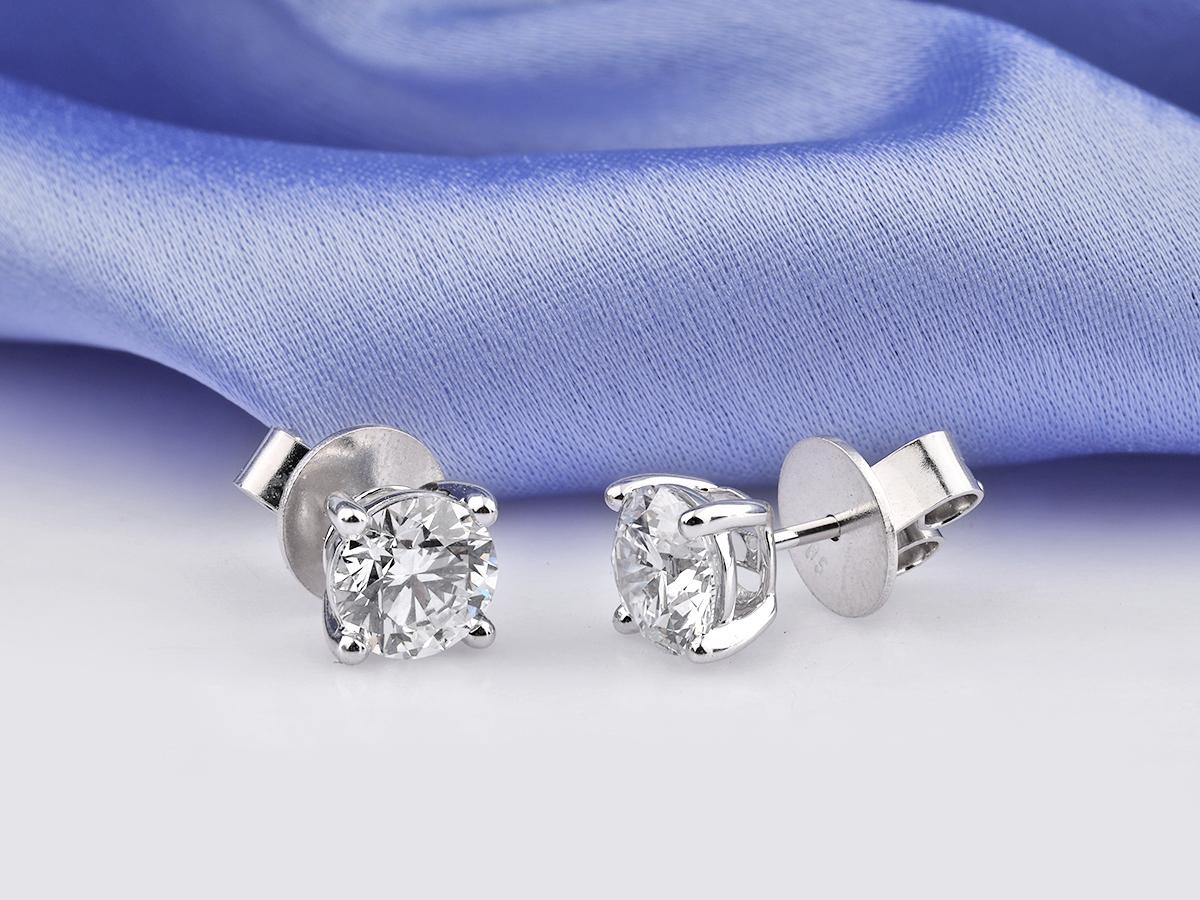 Ces élégantes boucles d'oreilles en or blanc 14 carats sont ornées de deux éblouissants diamants ronds naturels de taille brillant d'un poids total de 2,05 carats. Présentées dans un solitaire intemporel à quatre branches, les boucles d'oreilles