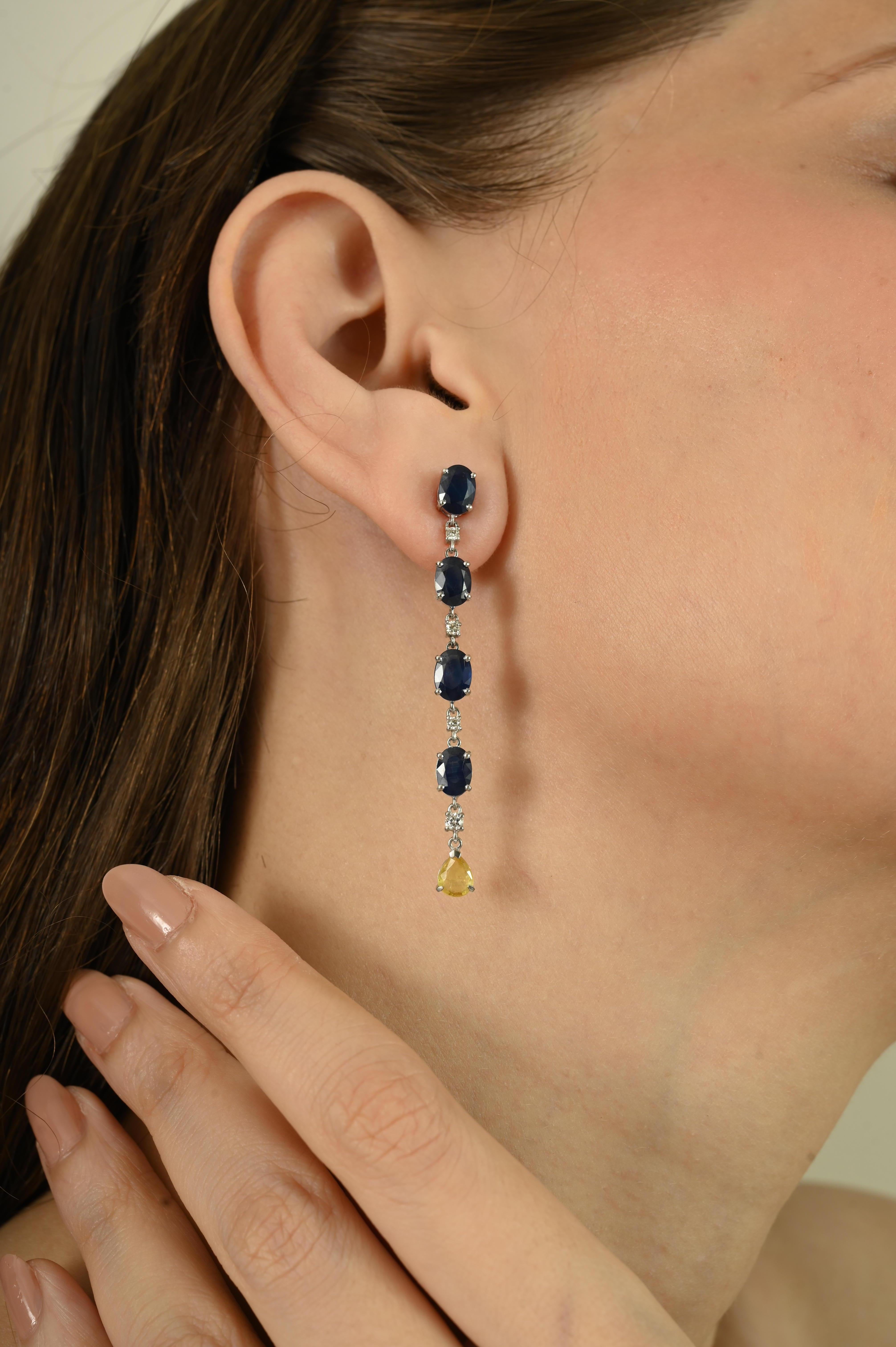Realizzati in oro bianco 14 carati, questi eleganti orecchini a goccia presentano 9,43 carati di zaffiri blu a taglio ovale e zaffiro giallo a taglio pera, accentati da 0,27 carati di diamanti rotondi a taglio brillante. Una goccia di zaffiro giallo