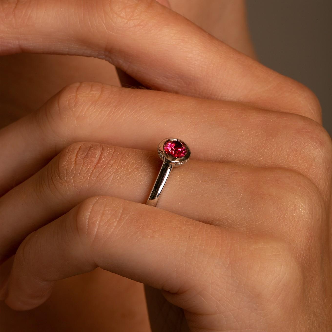 Questo anello presenta una tormalina ovale rosa brillante che cattura l'attenzione, incastonata in un castone orizzontale da est a ovest con un bellissimo diamante nascosto a raggiera per un'estetica decisamente moderna e fresca, con un tocco di
