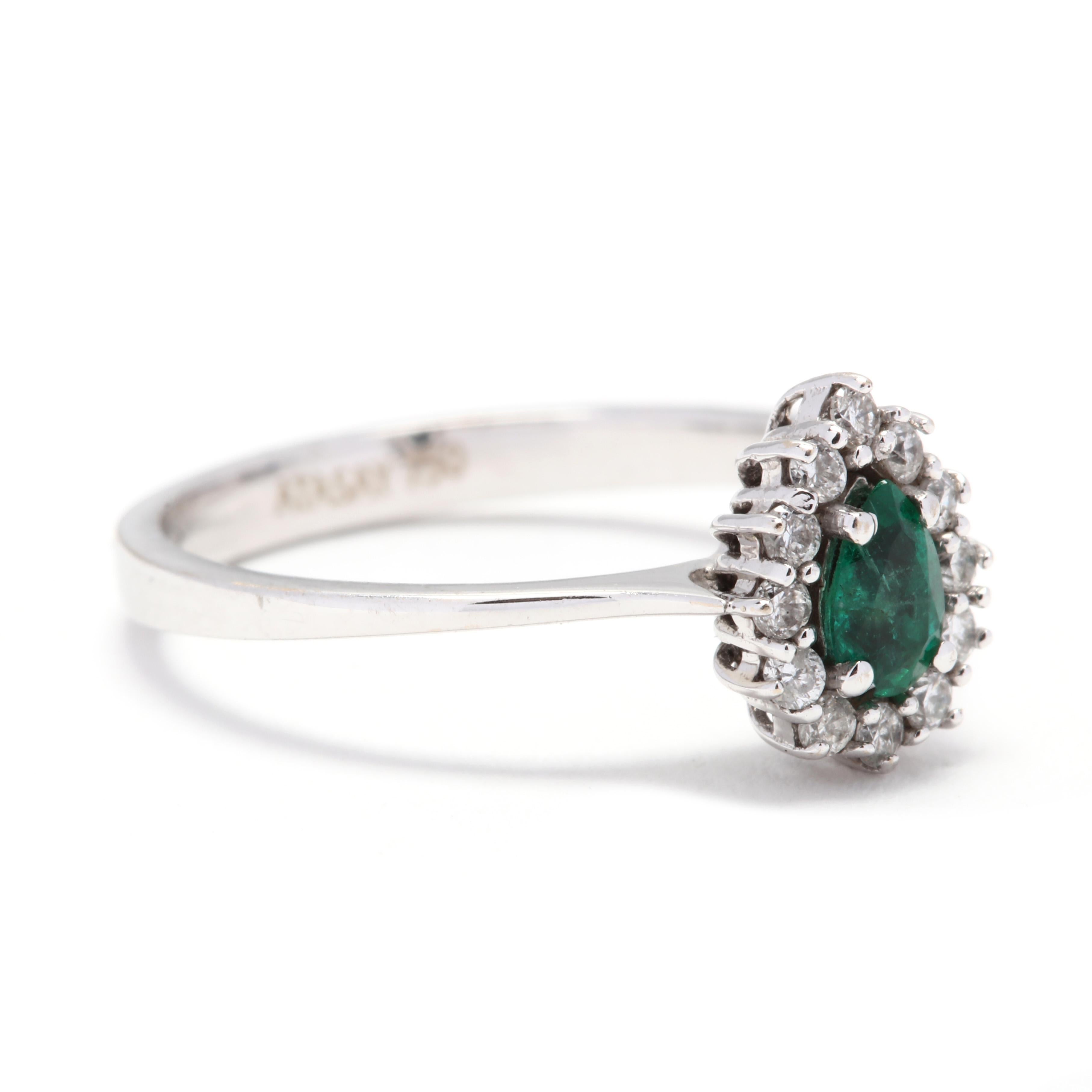 A 14 karat white gold, emerald and diamond ring. This ring features a prong set, pear cut emerald weighing approximately .21 carat surrounded by a halo of full cut diamonds weighing approximately .14 total carats and a thin, slightly tapered