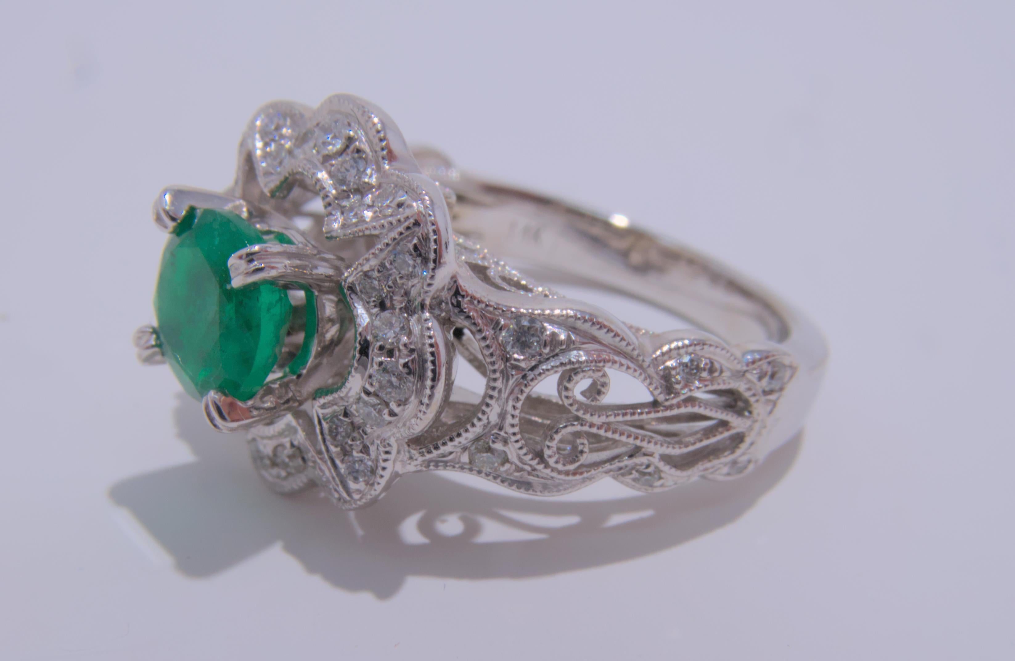This beautiful 14K white gold ring features a stunning round emerald at its center, surrounded by sparkling diamonds. The total estimated weight of the emerald is .77 carats, adding a pop of color and a touch of luxury to the piece. The diamonds,