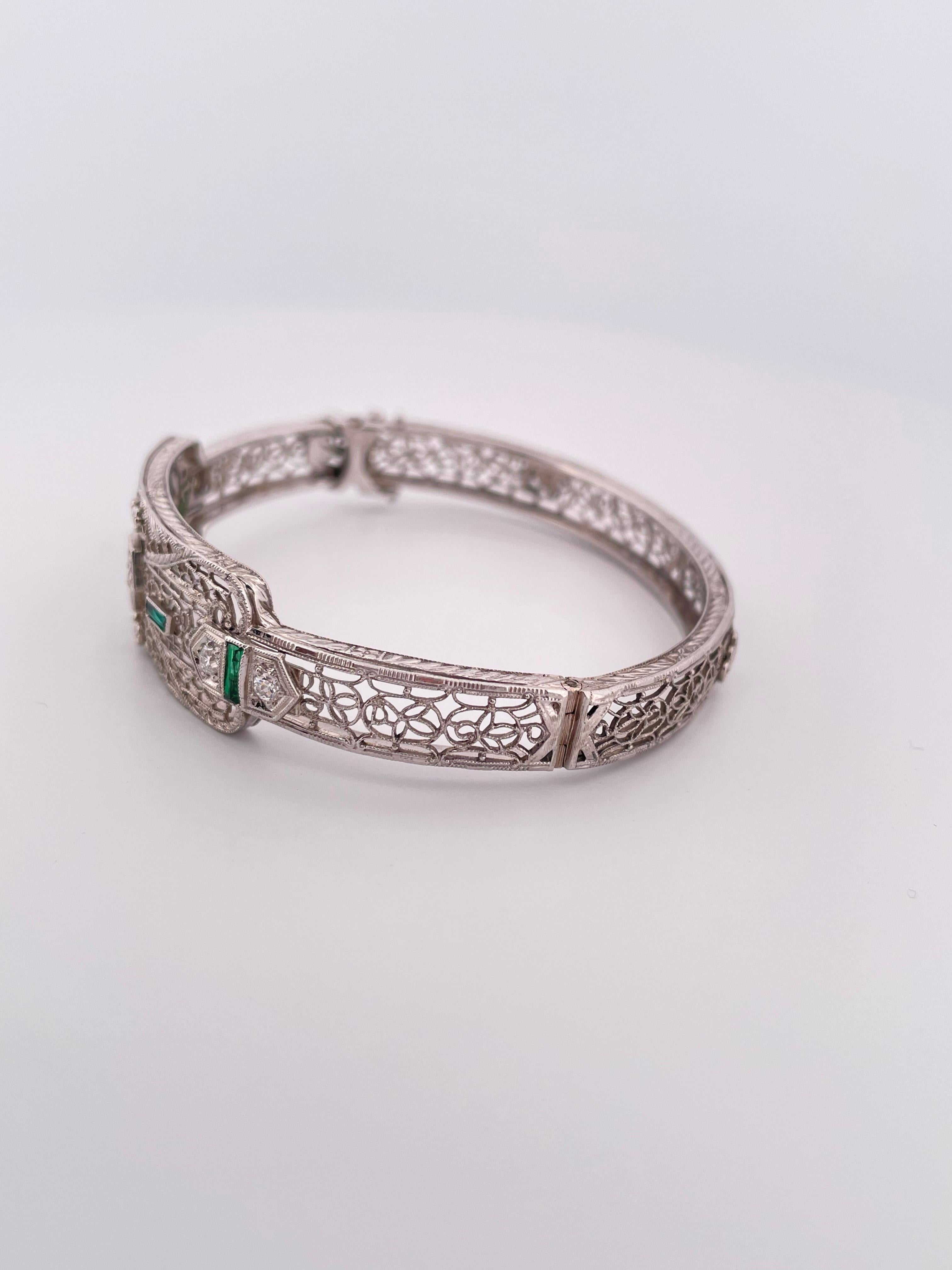 This exquisite Art Deco bracelet showcases timeless craftsmanship in platinum and 14k gold. Featuring intricate filigree detailing throughout, the centerpiece is adorned with sparkling diamonds and vibrant calibre-cut emeralds, creating a striking
