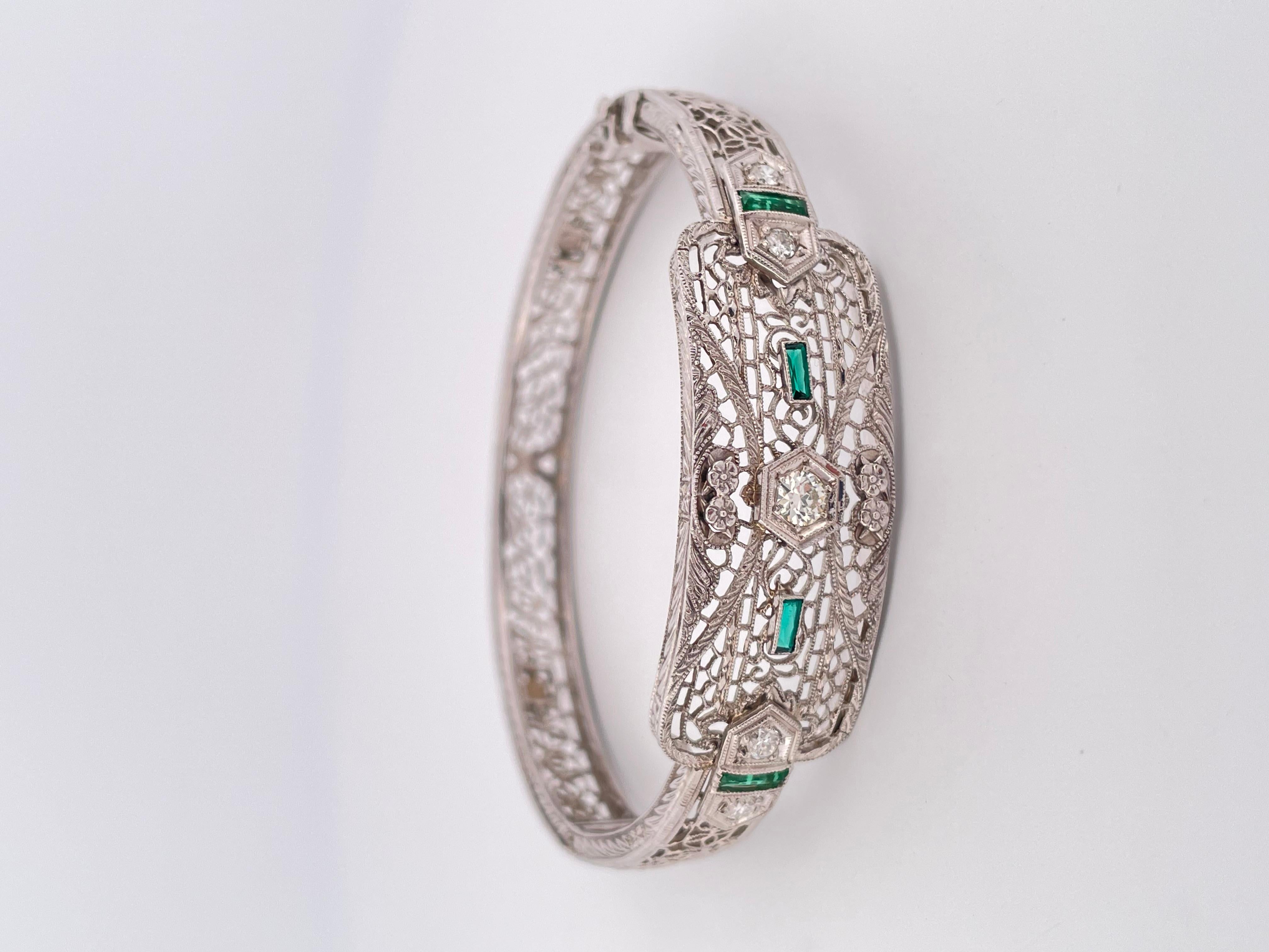 This exquisite Art Deco bracelet showcases timeless craftsmanship in platinum and 14k gold. Featuring intricate filigree detailing throughout, the centerpiece is adorned with sparkling diamonds and vibrant calibre-cut emeralds, creating a striking