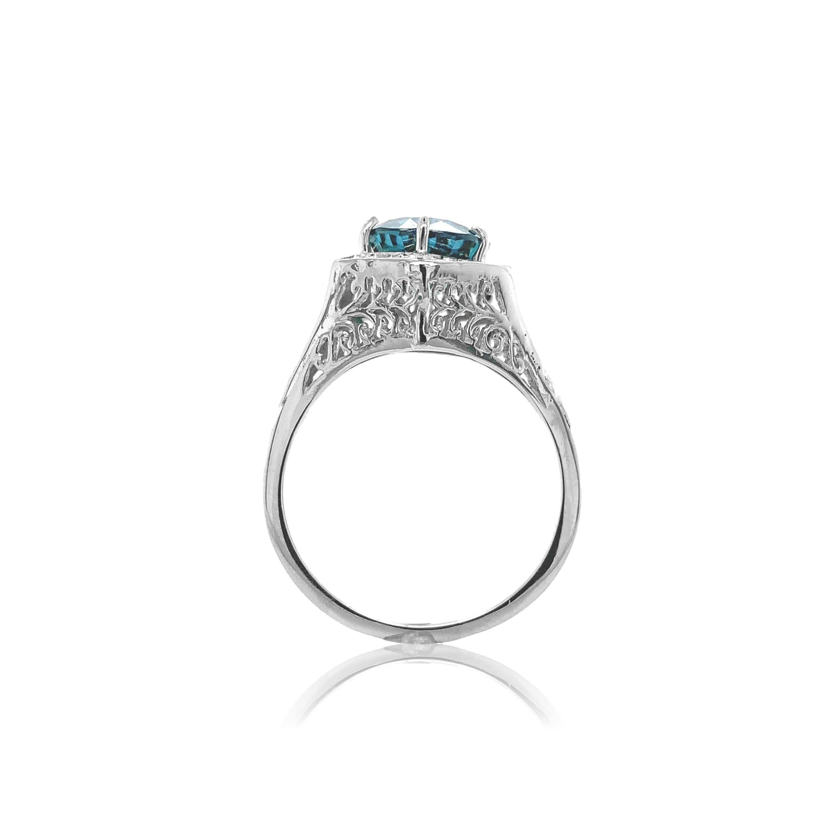 14K white gold filigree ring featuring a round brilliant cut teal blue-green zircon. The zircon measures about 8.5 and has lots of extra faceting. Blue zircon is a naturally mined gemstone found primarily in Cambodia. Zircon has a high refractive