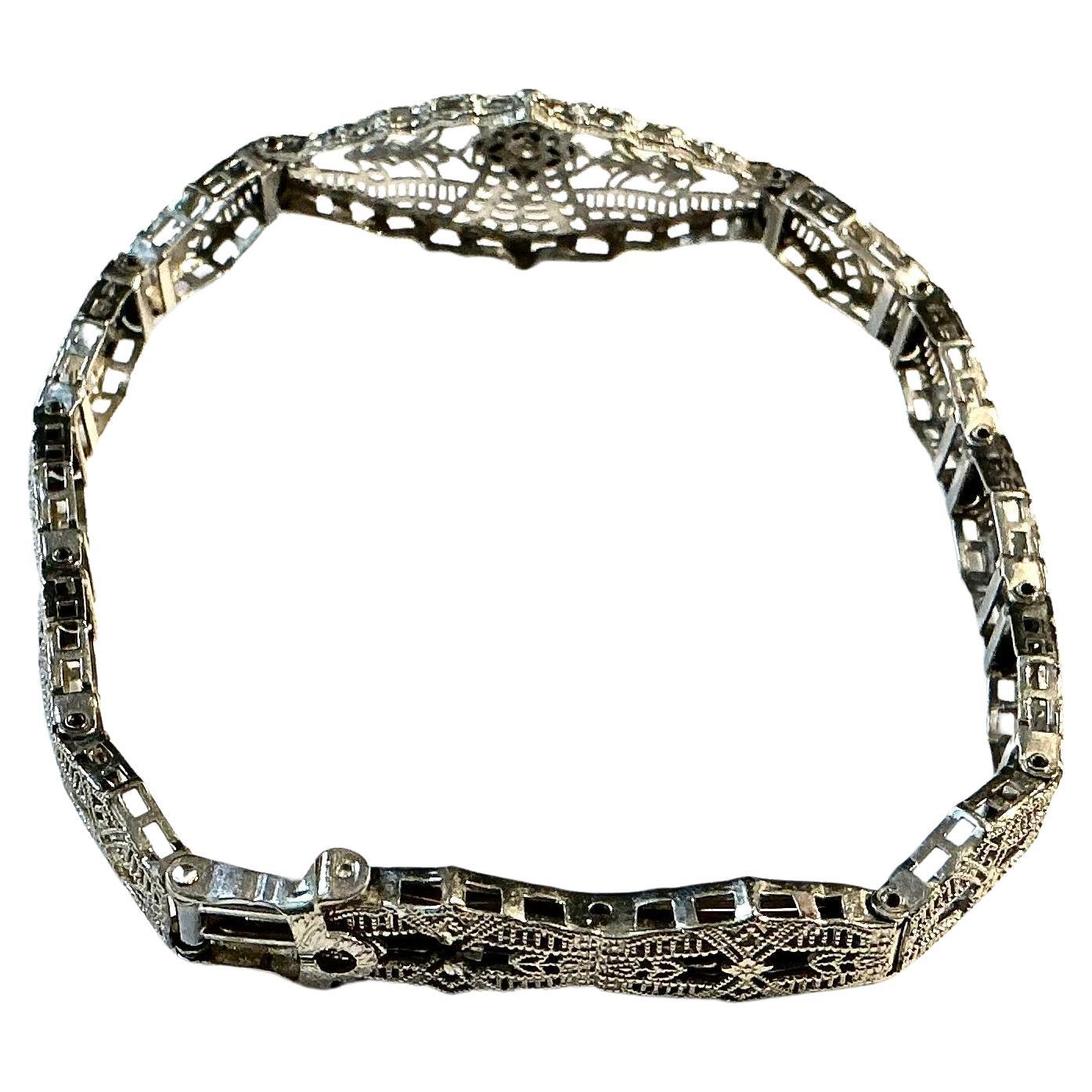 Early 20th Century White Gold and Diamond Filigree Art Deco Bracelet. Bracelet features delicate openwork and a subtle geometric design. At the center is a single small diamond, bezel-set in a rhombus-shaped cartouche that radiates outward with