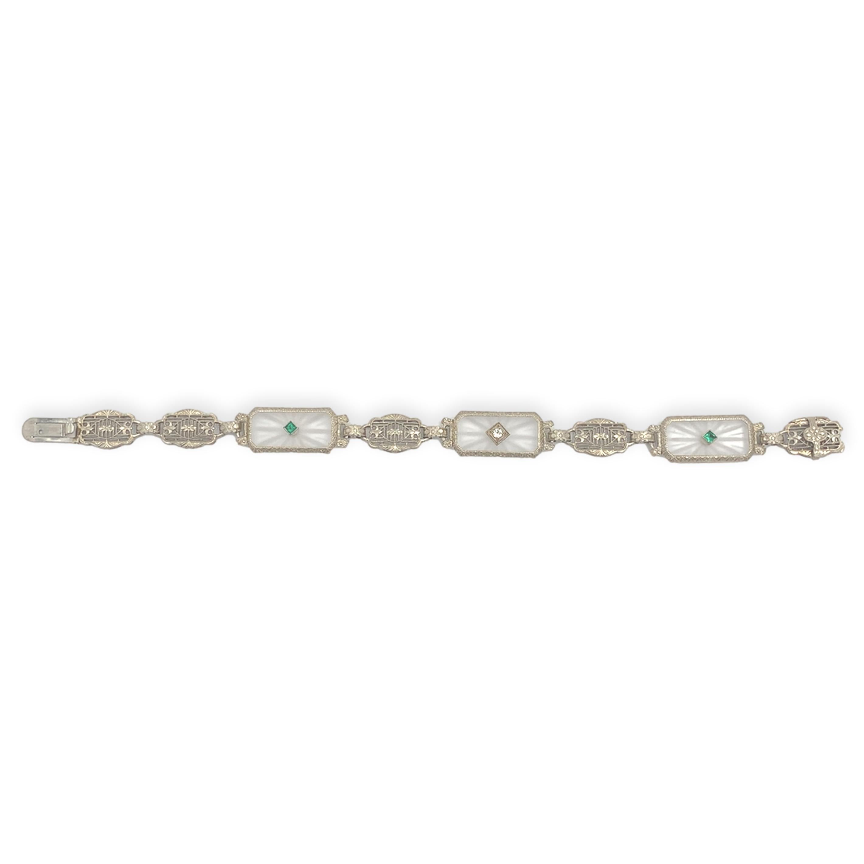 Art Deco 14K white gold filigree bracelet featuring 3 rock crystal quartz panels. One rectangular quartz is set with a diamond and the other 2 are set with square synthetic/glass green stones.  The frosted and reverse carved crystals measure about