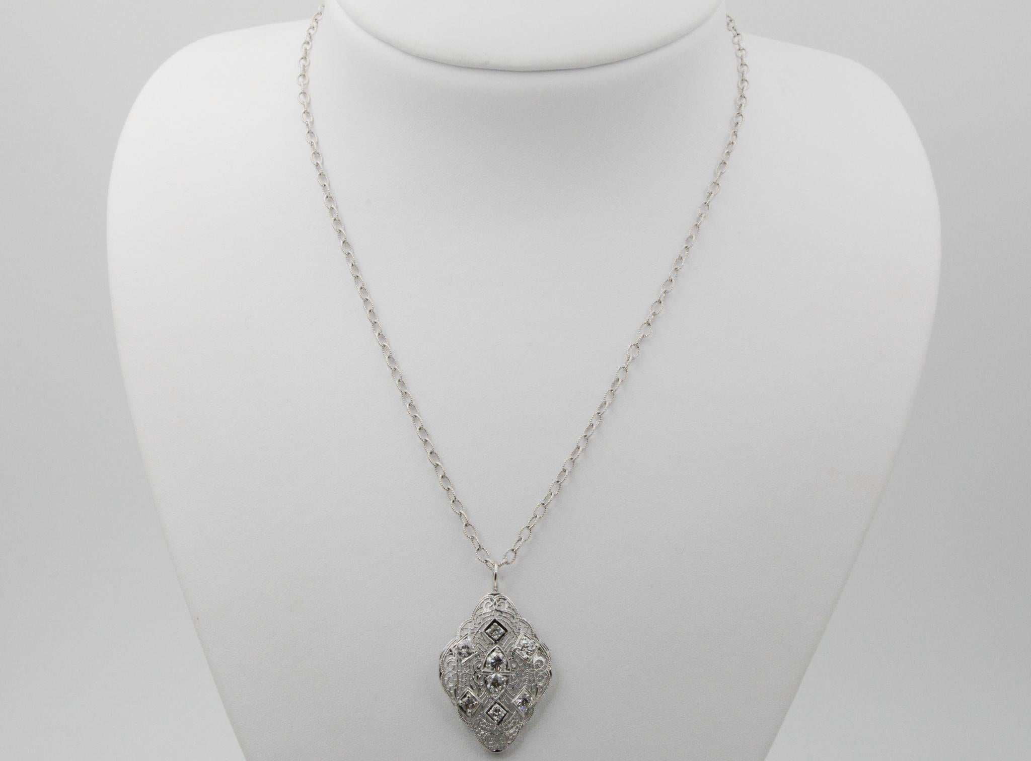 This 14 karat white gold filigree pendant features a dazzling vintage design with eight old European cut diamonds, weighing approximately 1.50 carats. The diamonds have I-J coloring and SI-I1 clarity. The pendant has an oval design with slightly