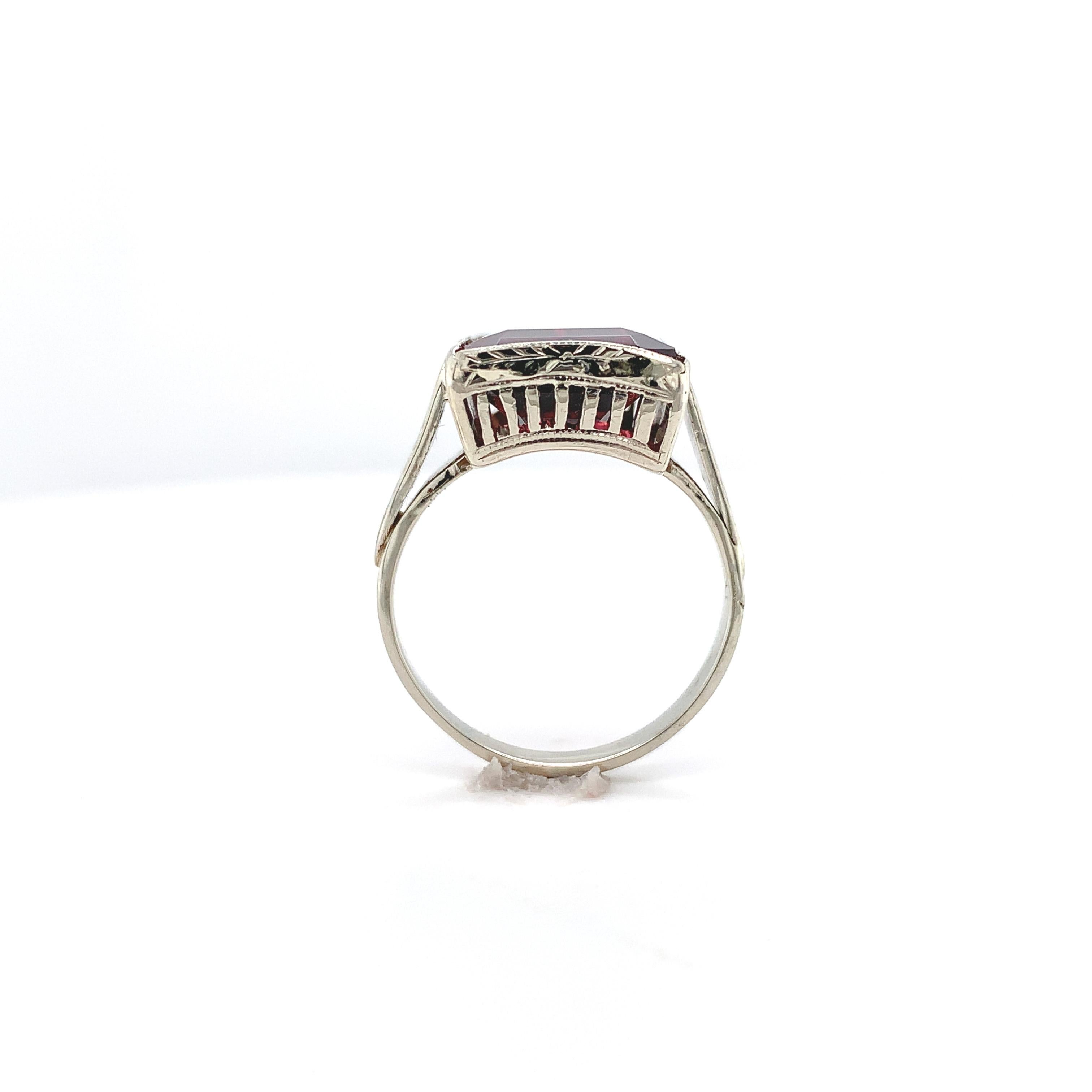 Vintage 14K white gold ring featuring an emerald cut rhodolite garnet. This deep raspberry dark pinkish-red color garnet weighs 8.35 carats and measures about 14mm x 10mm. The mounting is all hand engraved. The ring originally accommodated a square