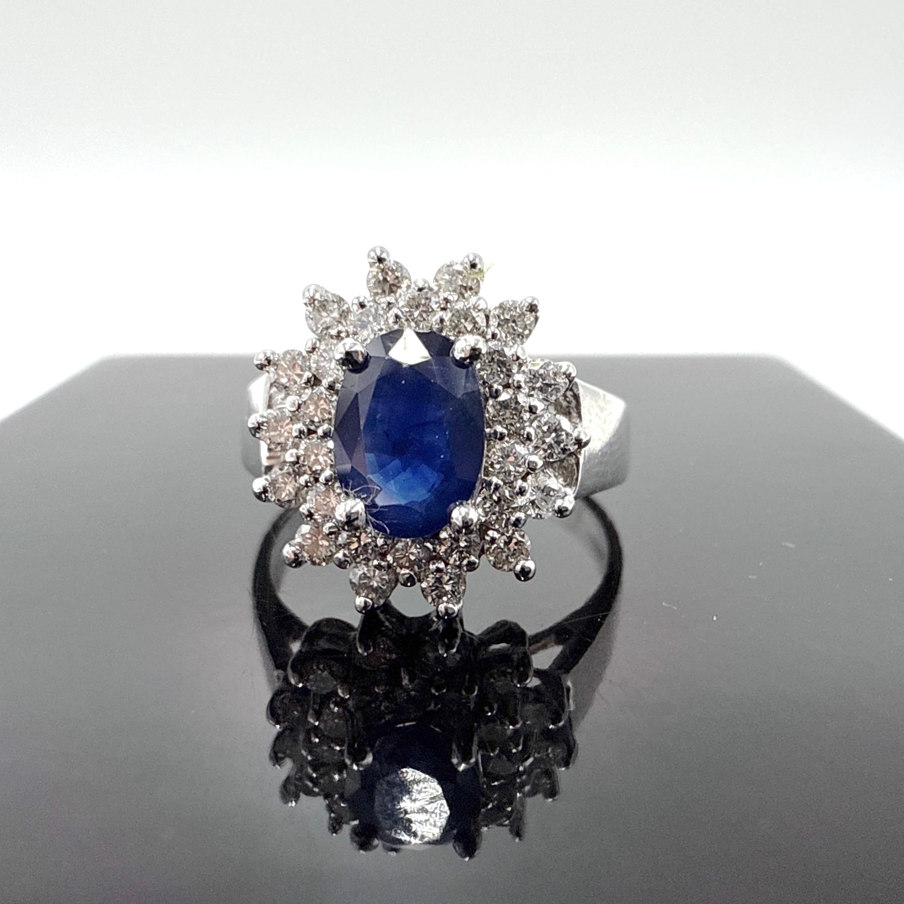 Questo elegante anello a grappolo è realizzato in oro bianco 14K e presenta uno zaffiro blu centrale dal taglio ovale del peso di circa 0,87 carati. Lo zaffiro misura circa 7,05 mm x 5,09 mm x 2,47 mm e presenta una tonalità mediamente scura con una