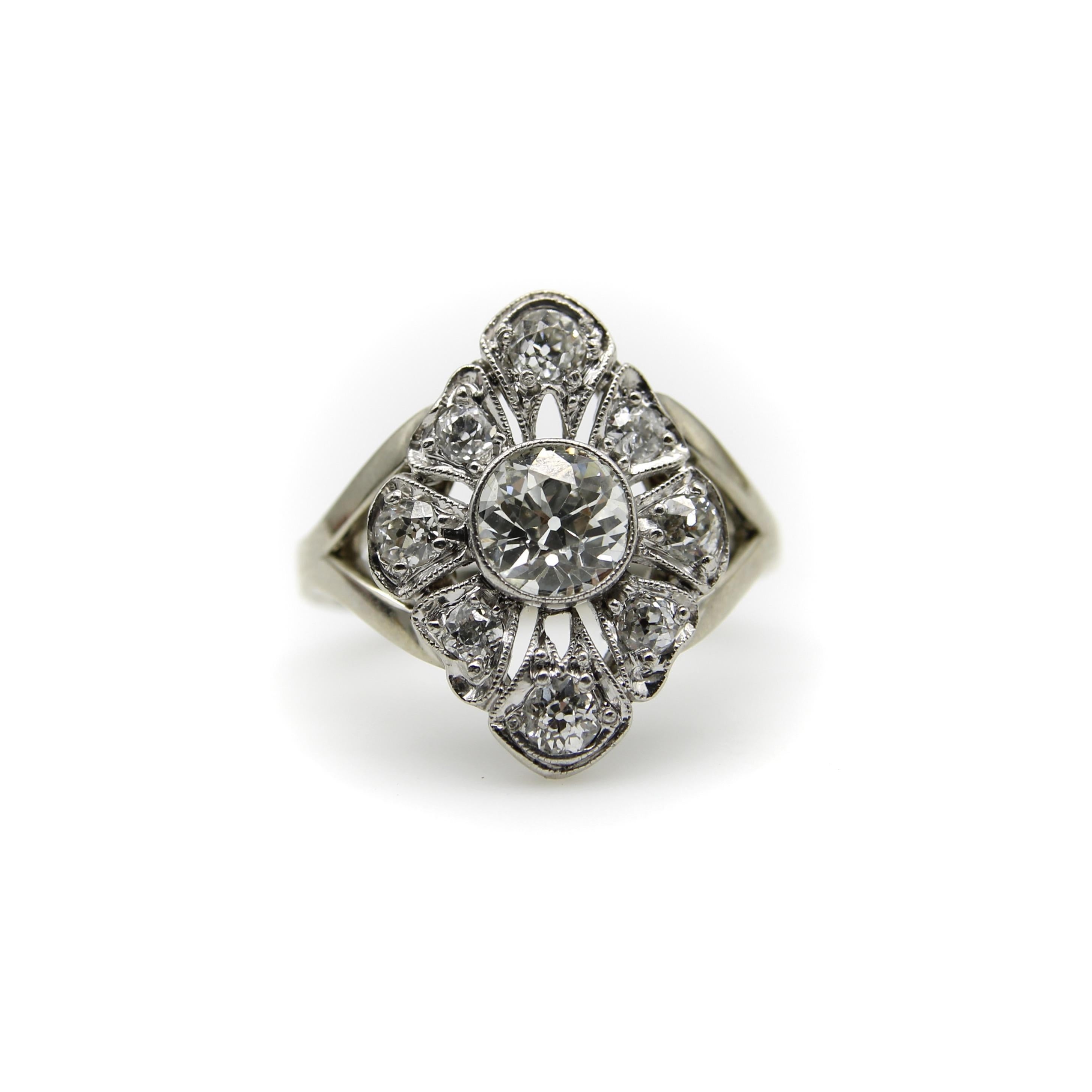 Este precioso anillo floral gira en torno a un diamante de talla europea antigua, con ocho apéndices en forma de pétalo que crean la forma de una flor. El diamante central tiene poco menos de un quilate, con un hermoso brillo que atrae la mirada