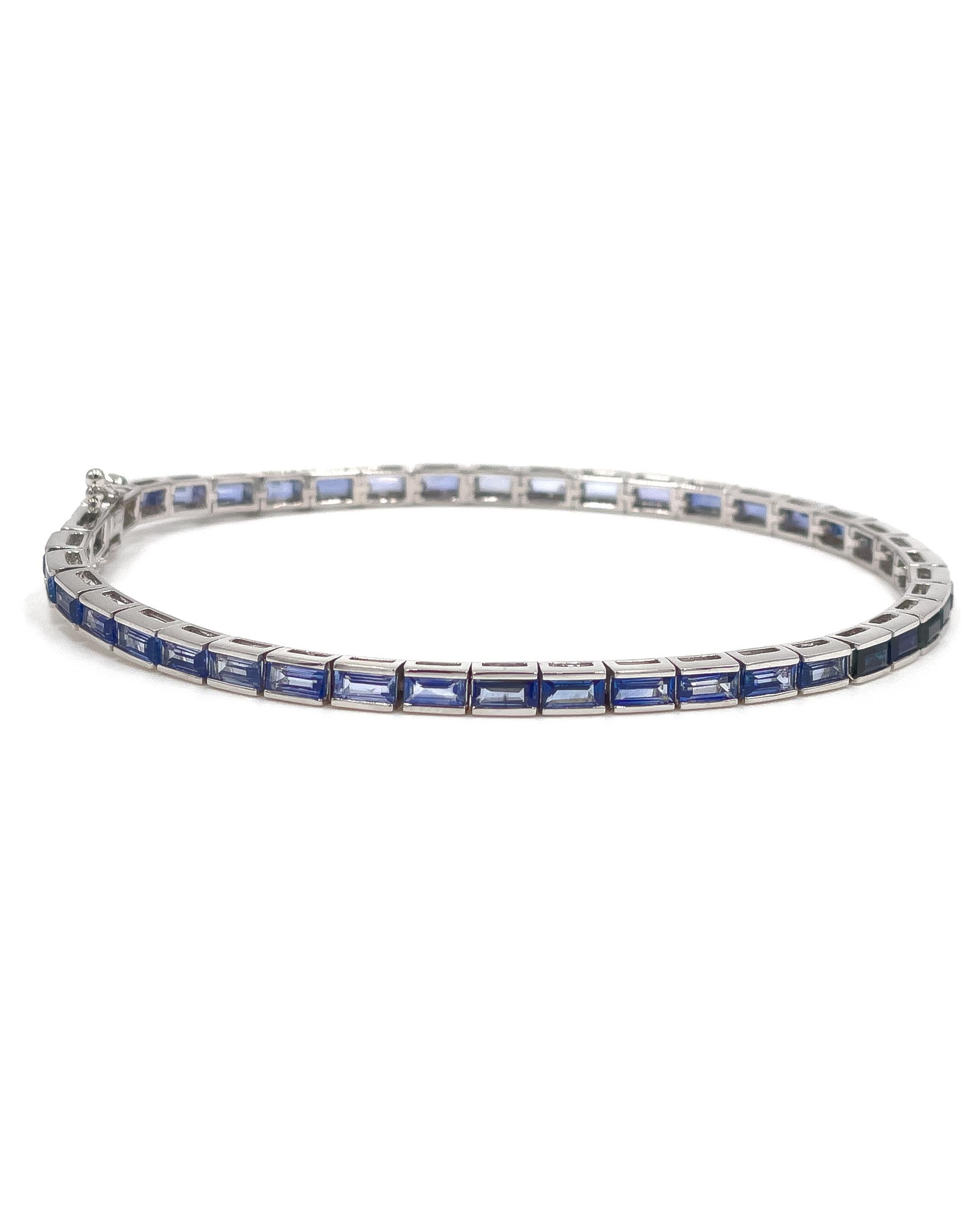 14K white gold line bracelet channel set with step-cut blue sapphires graduating in color. 

The sapphires weigh a total of 6.23 carats. 

The bracelet has a box clasp with two figure 8 safety clasps on either side.

Bracelet length: 7 inches.
