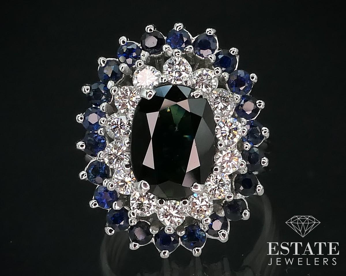 Jaw dropping ladies cocktail ring with natural blue sapphires and diamonds in a ballerina style double halo setting. At the center is a 10mm by 7mm deep and rich colored blue sapphire with approximately 2ctw of natural diamonds and sapphires around