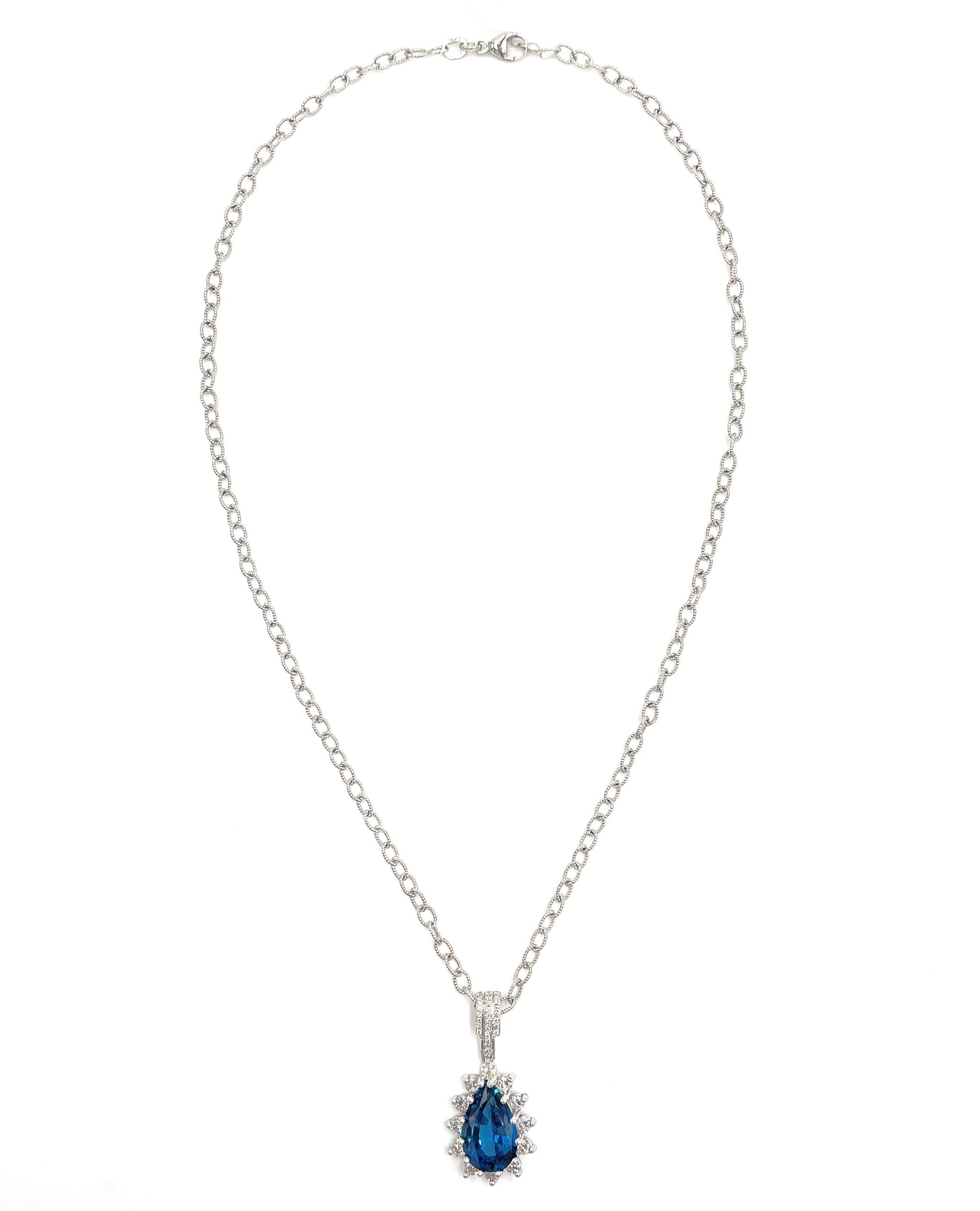 14K white gold pendant furnished with 12 round prong set diamonds weighing 0.62 carats total (G/H color, VS2/SI1 clarity) and 26 round diamonds weighing approximately 0.20 carats total (H color, SI clarity). In the center, one pear shape London blue