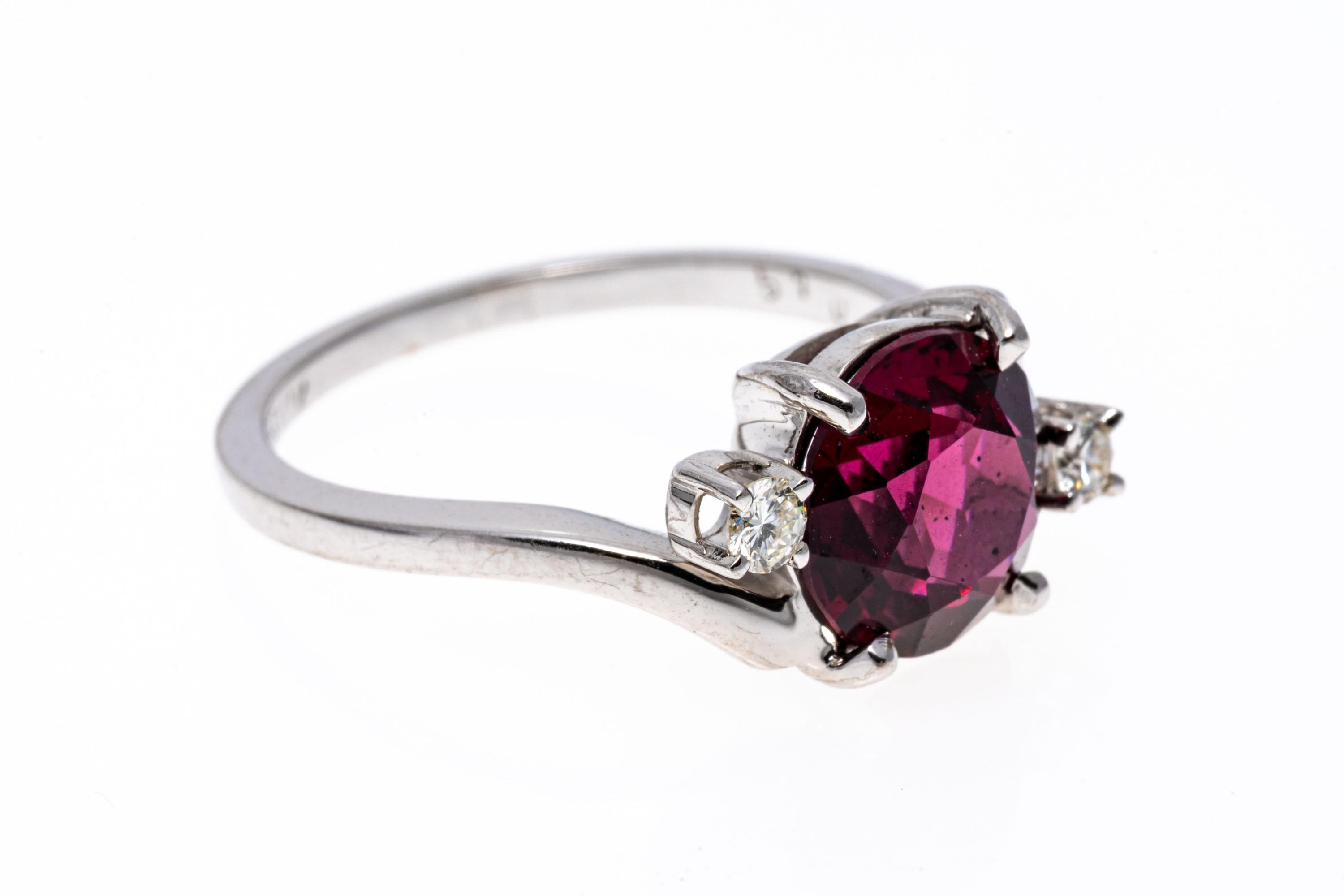 14k white gold ring. This pretty white gold bypass style ring is set with a center round faceted, purplish red color rhodolite garnet, approximately 2.26 CTS, prong set. The garnet is flanked with offset round faceted diamonds, approximately 0.08