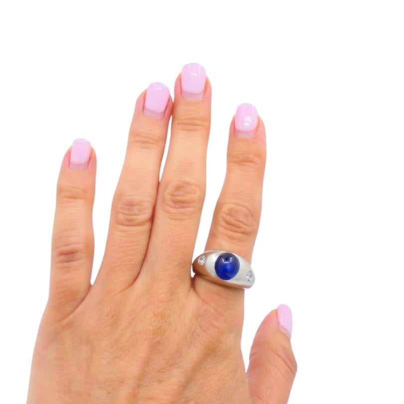 Bague en or blanc 14k de l'époque Art déco, ornée d'un saphir cabochon et d'un diamant.
Le saphir a un éclat riche et brillant, qui donne à la bague une douce luminosité. Le cabochon est flanqué de deux diamants ronds. La monture a une forme