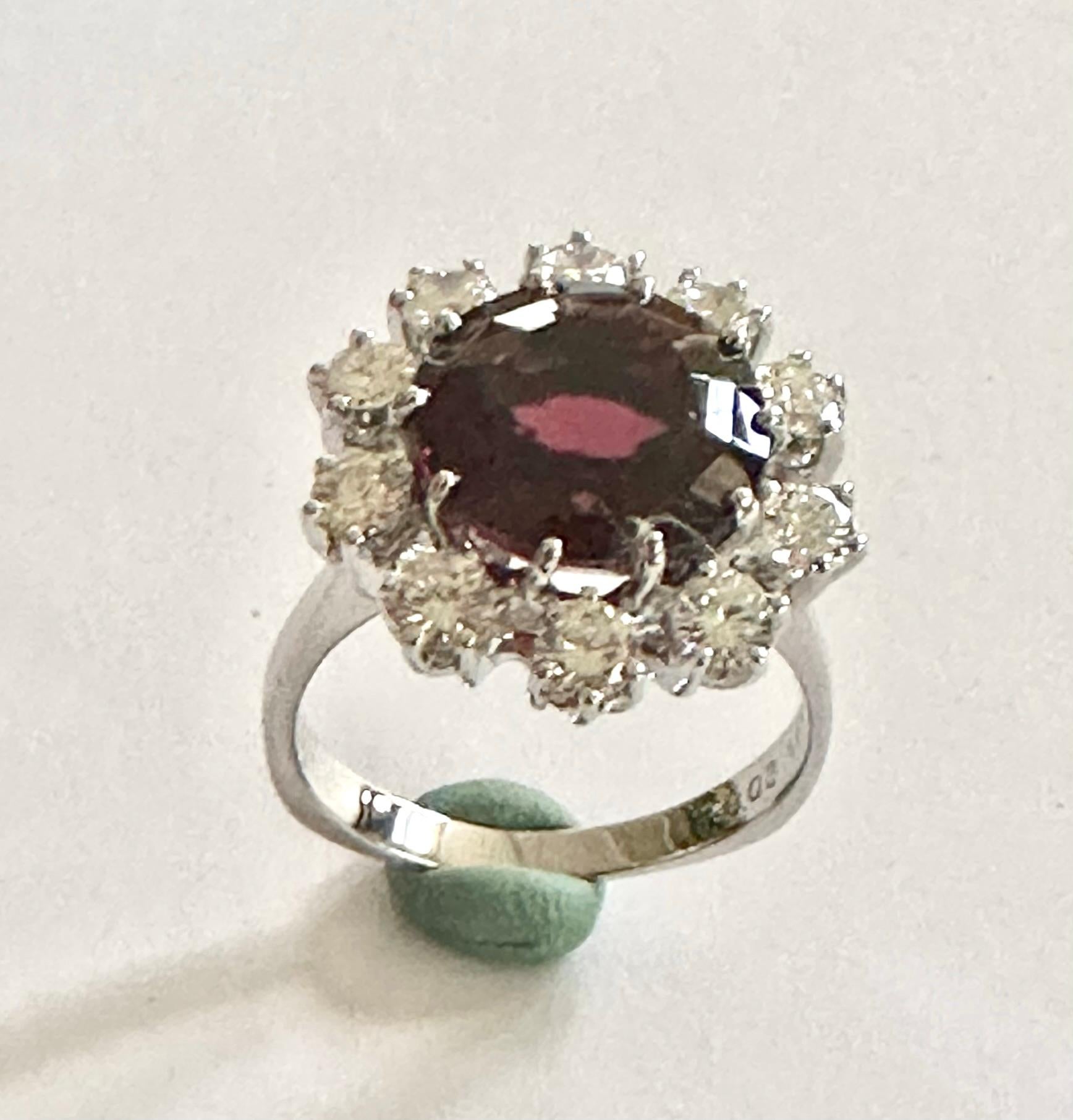 One (1) 14K.  white  Gold entourage Ring made in Germany 1965 By Eduard G. Fidel  Pforzheim
Set with One Natural Garnet; RHODOLTE weightof : 8.08 ct.  in round Mixed Cut
+  10 brilliant Cut Diamonds of total weight: 1.23 ct  VS-F 
Size of the ring:
