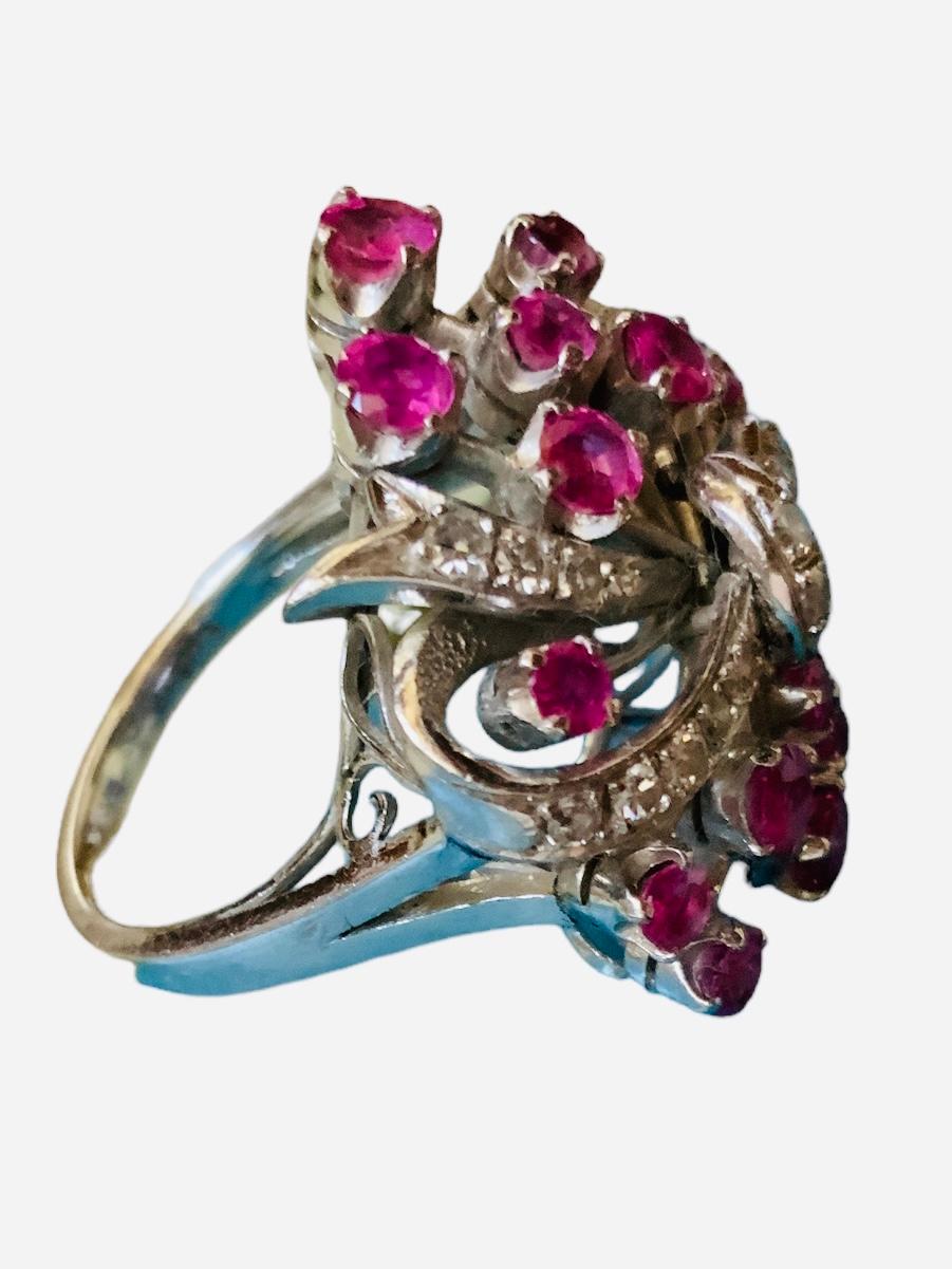 This is a 14K white gold rubies ring. It depicts a “bouquet of flowers” made of rubies on prong setting and adorned with a large bow. It is hallmarked 14K inside the shank.