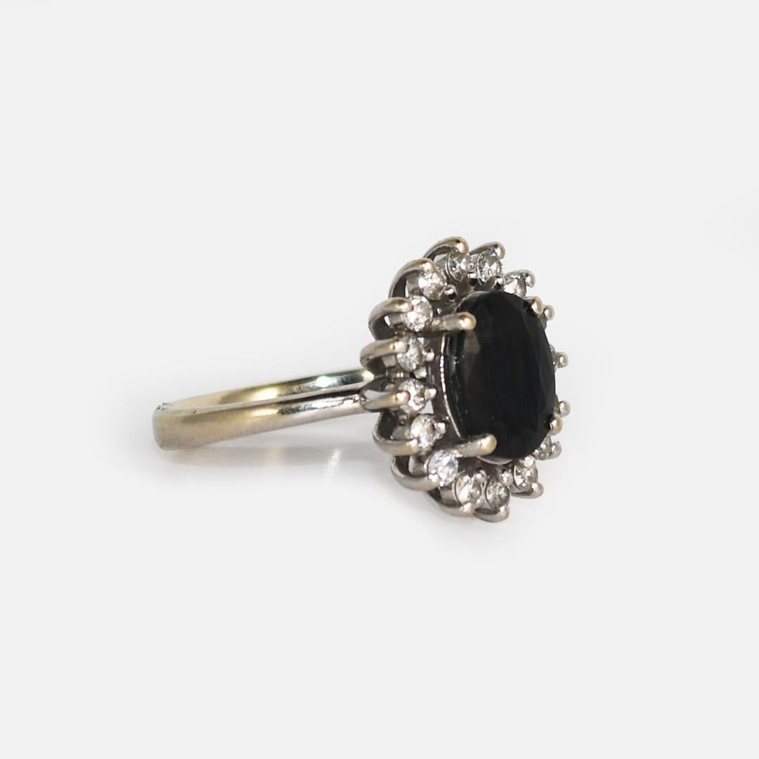 The center stone is a Natural Dark Blue sapphire measuring 8.8mm x 7.5mm, Surrounding the Sapphire are 18 .02ct Diamonds. 
Si1 - Si2 Clarity - G-H Color. .36tdw
Set in 14k white gold
weighs 4.2gr
Size 7 1/2
Can be resized up or down for an