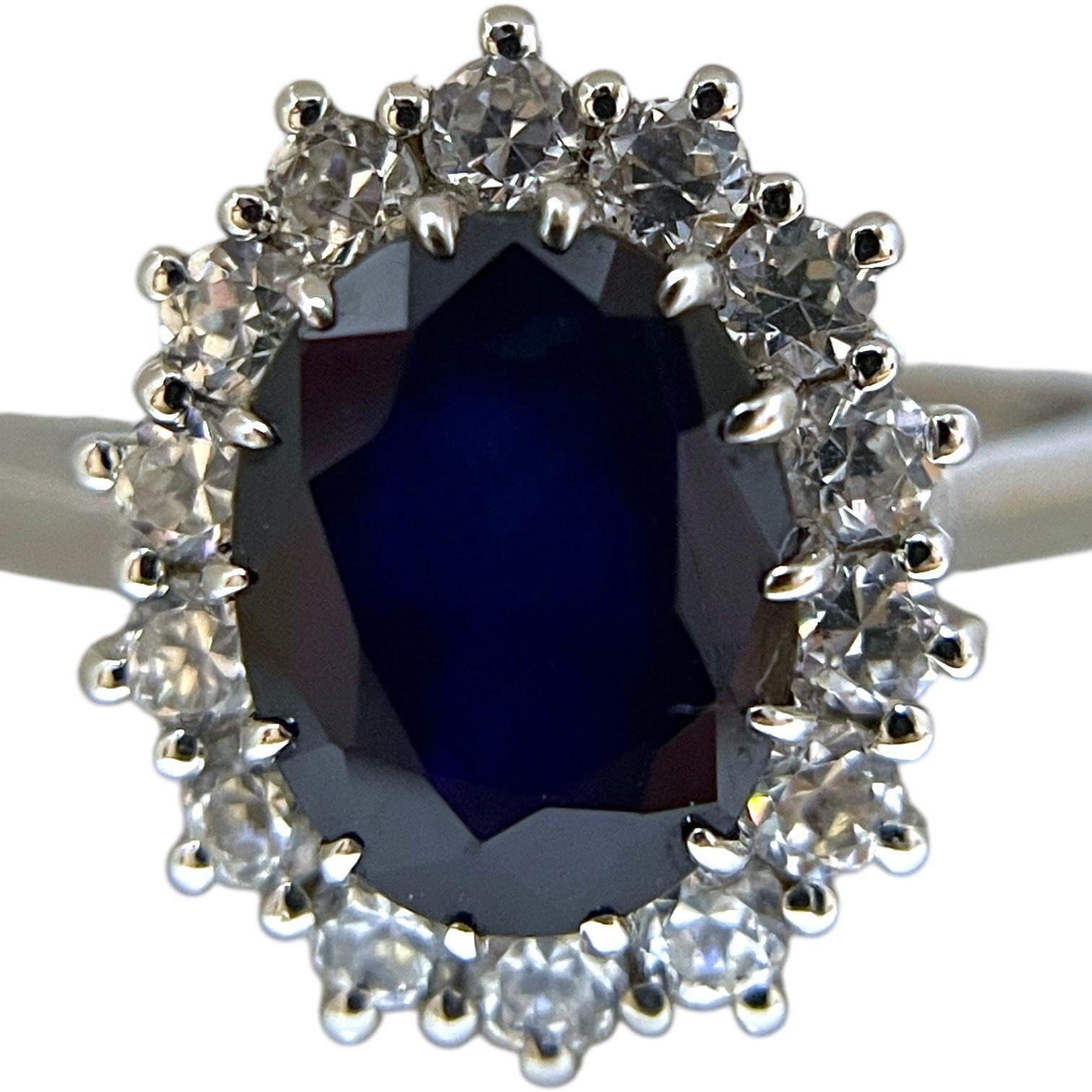 A stunning 14K white gold ring featuring a deep blue oval-cut sapphire as its centerpiece, surrounded by a radiant halo of brilliant-cut diamonds. Reflecting the regal style of the mid-20th century, this design exudes timeless sophistication and
