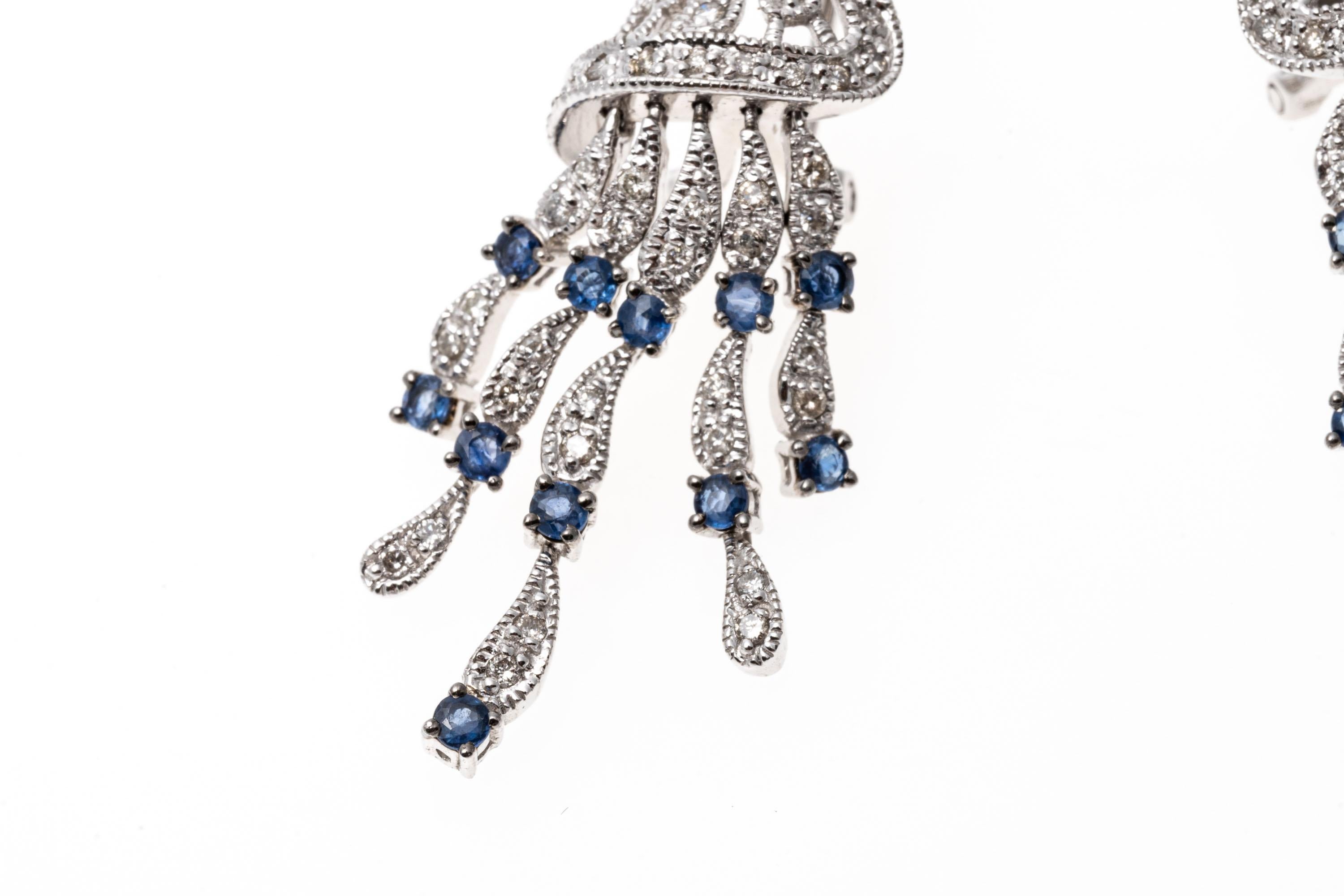 Crafted of 14K white gold, these dynamic earrings showcase an opposing design set with diamonds. Suspended from the base of the earrings are five graduated tassels of diamonds and bright blue sapphires. The diamonds are approximately 0.74 TCW and