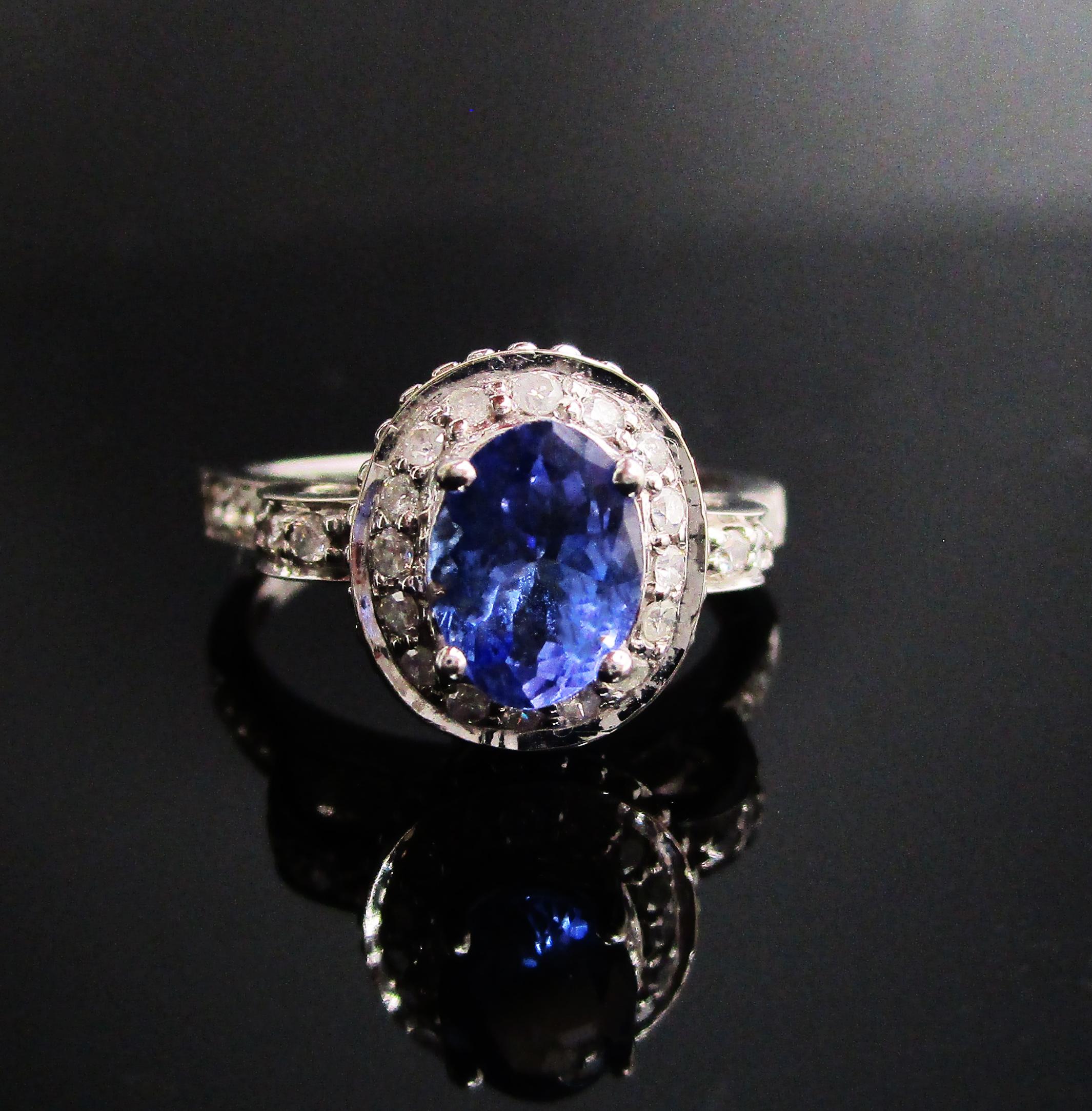 This is a stunning 14k white gold engagement ring with a tanzanite center stone, diamond accents, and beautiful filigree details. The ring has a fantastic depth and a dramatic setting. The tanzanite center is surrounded by a frame of diamonds that