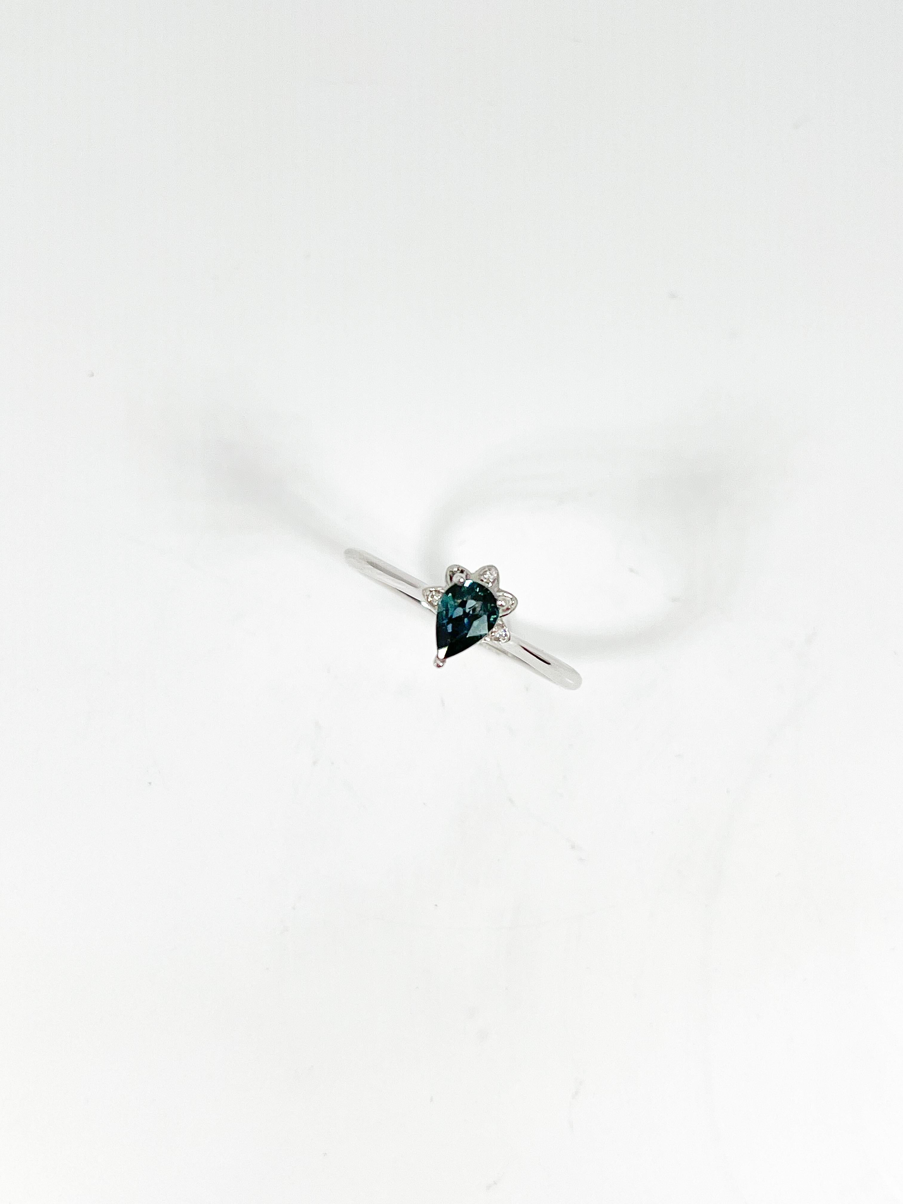 14k white gold ring with a teal pear sapphire center stone with a .50 CTW diamond flower design that goes underneath the sapphire. The center stone has a measurement of 6.5 x 4.2, the ring is a size 7, and has a total weight of 2.15 grams.