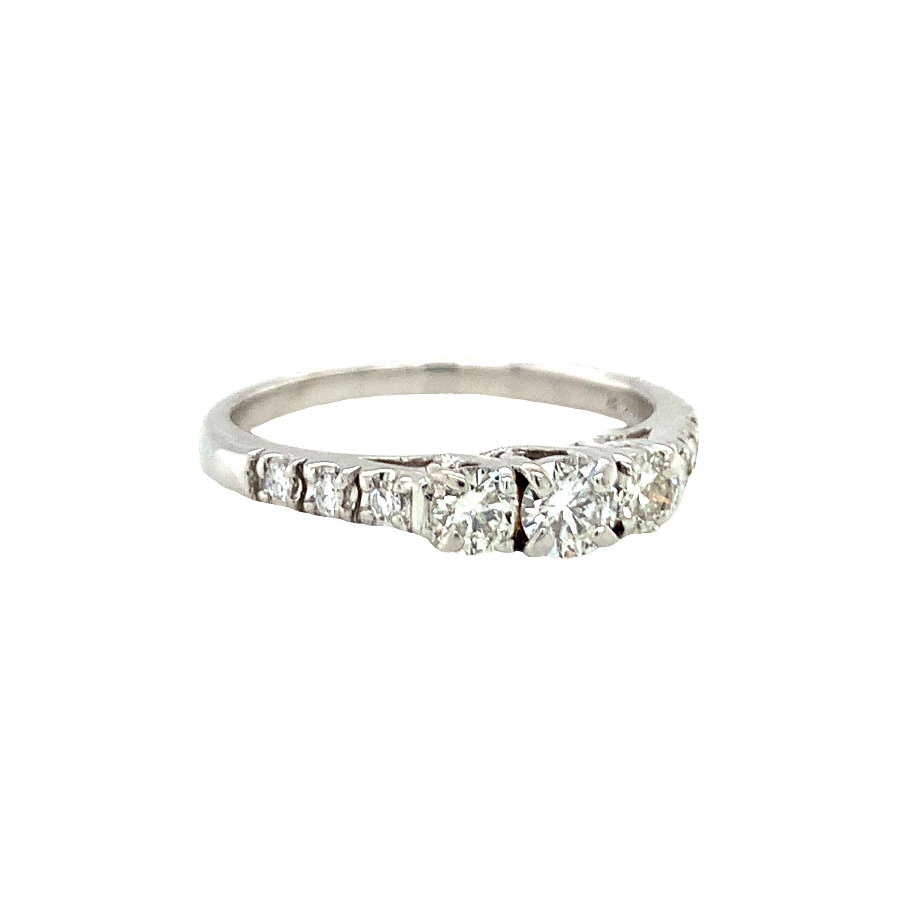 Une bague à trois pierres en or blanc 14 carats centrée sur trois diamants ronds de taille brillant sertis clos totalisant 0,43 ct (0,17 ct + 0,13 ct + 0,13 ct) de couleur H et de pureté SI-1. Les épaules sont ornées de 6 diamants ronds totalisant