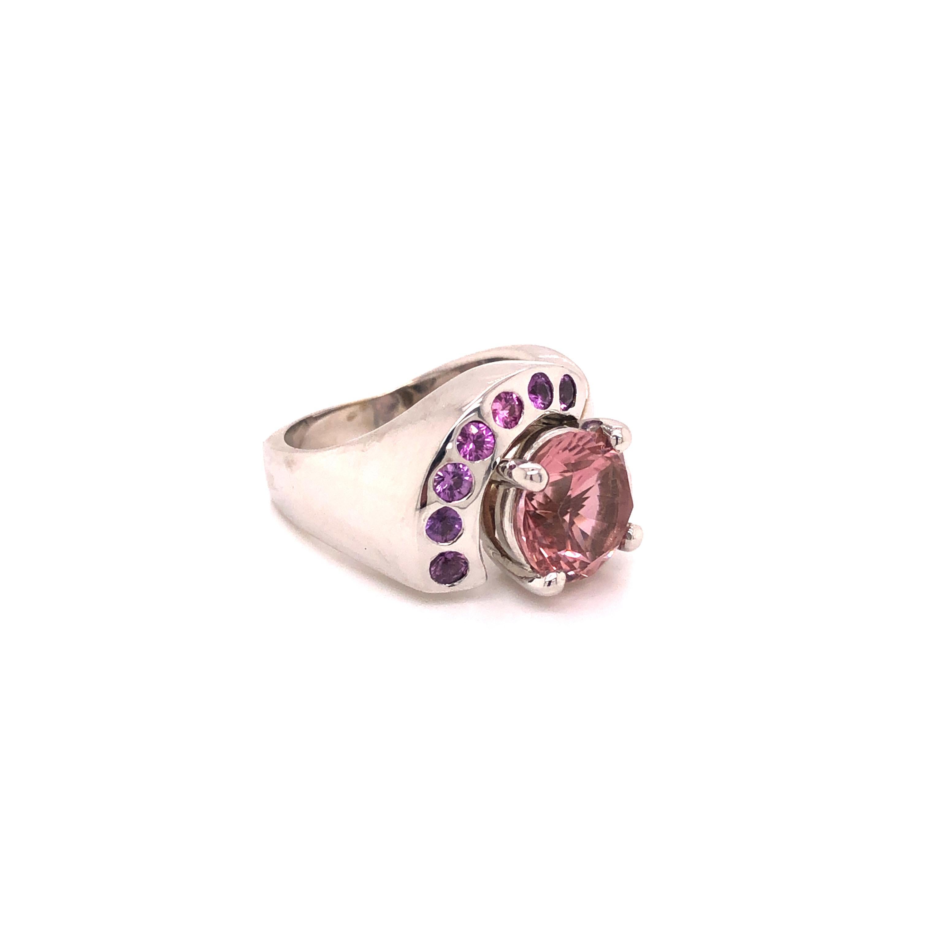 A vintage 14K white gold ring containing a round-cut pink tourmaline measuring 9.48 - 9.56 x 6.25 mm and weighing 3.26 carats, enhanced by round-shaped pink sapphires weighing a total of 0.50 carat.

Stone: Tourmaline, Pink Sapphire

Metal: 14K