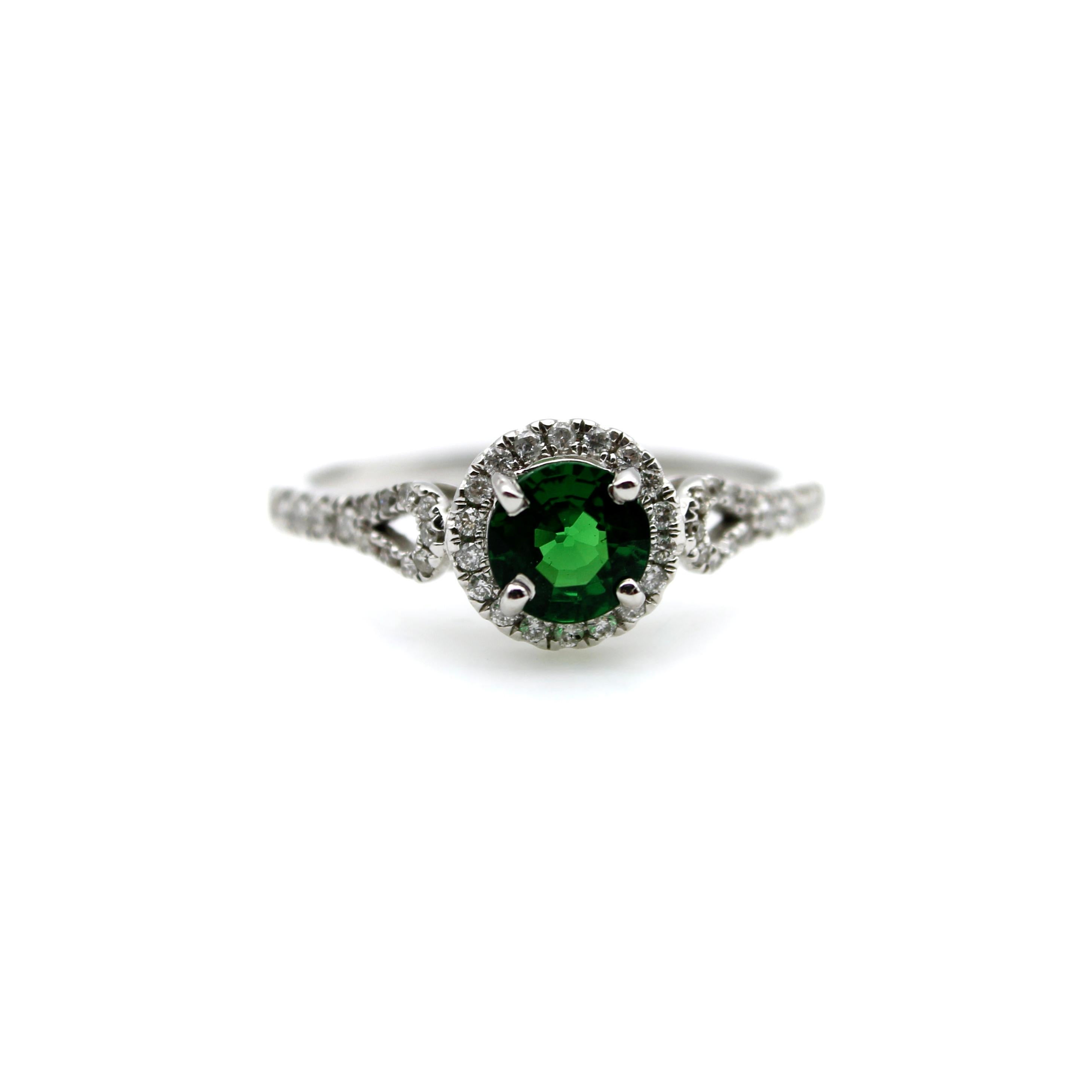 This gorgeous 14k white gold ring features a vibrant green Tsavorite Garnet, surrounded by a halo of diamonds. The green gemstone is a deep, yet bright, green that reflects the light beautifully, and its color pops against the white backdrop of