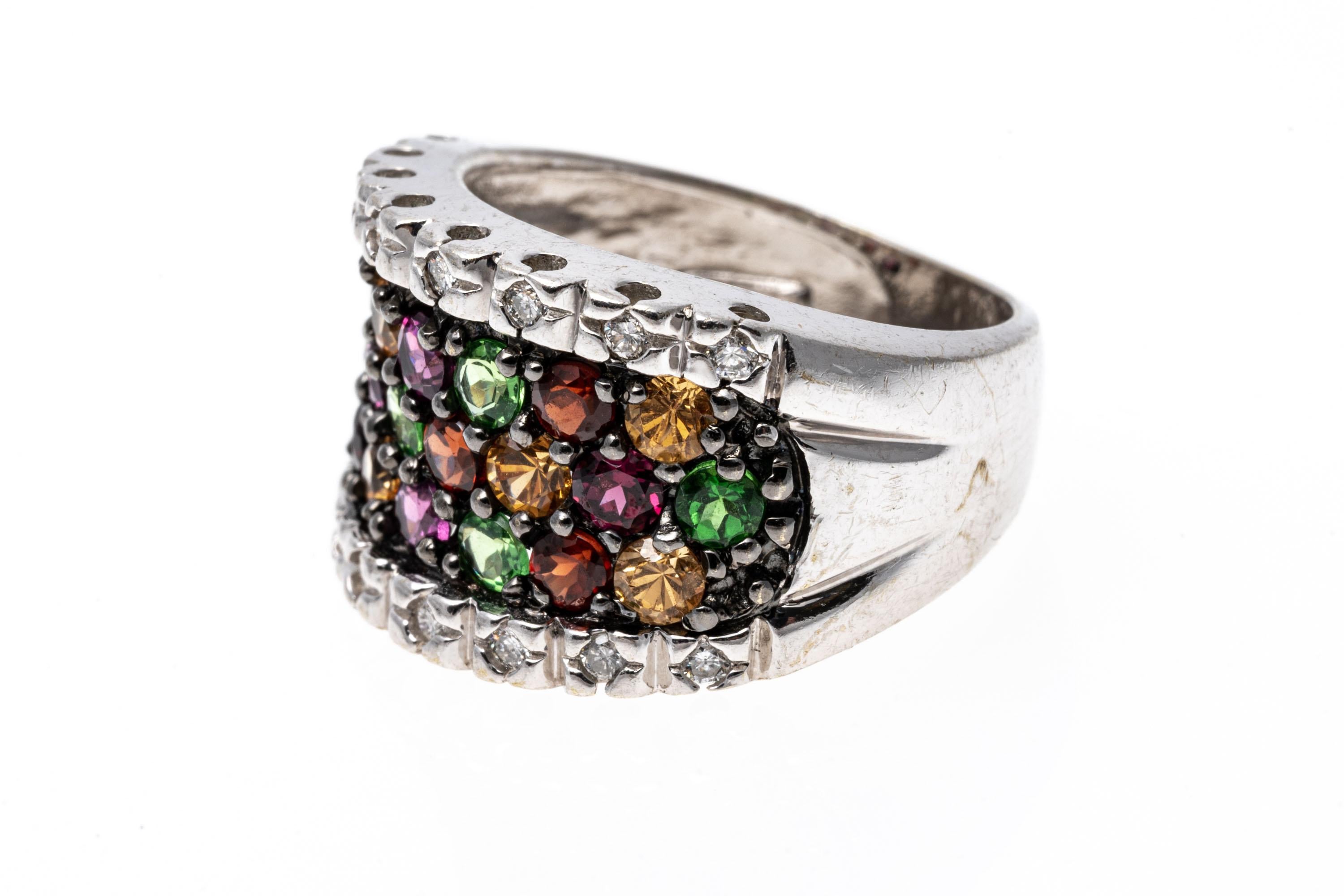 A cluster of round cut garnets in a brilliant array of reds, yellows, greens and pinks trail over the face of this dynamic 14K white gold ring. To either side of the garnets is a row of diamonds that creates a brilliant flash. Garnets approximately