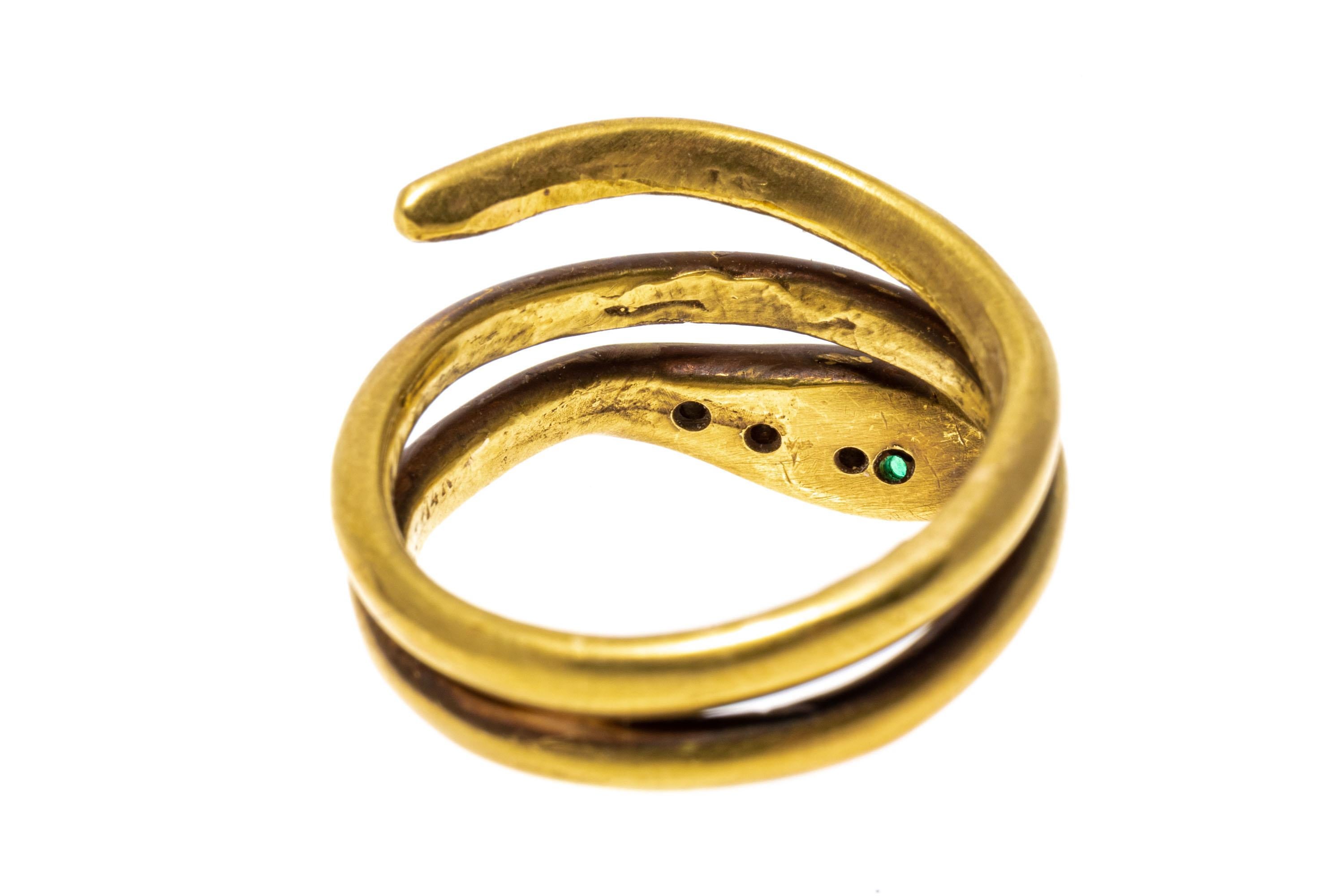 This unusual ring is a coiled snake motif with a burnished finished body, wound into a double coil and finished with round faceted emerald set eyes, approximately 0.04 TCW and three graduated, round faceted diamonds flush set into the head,