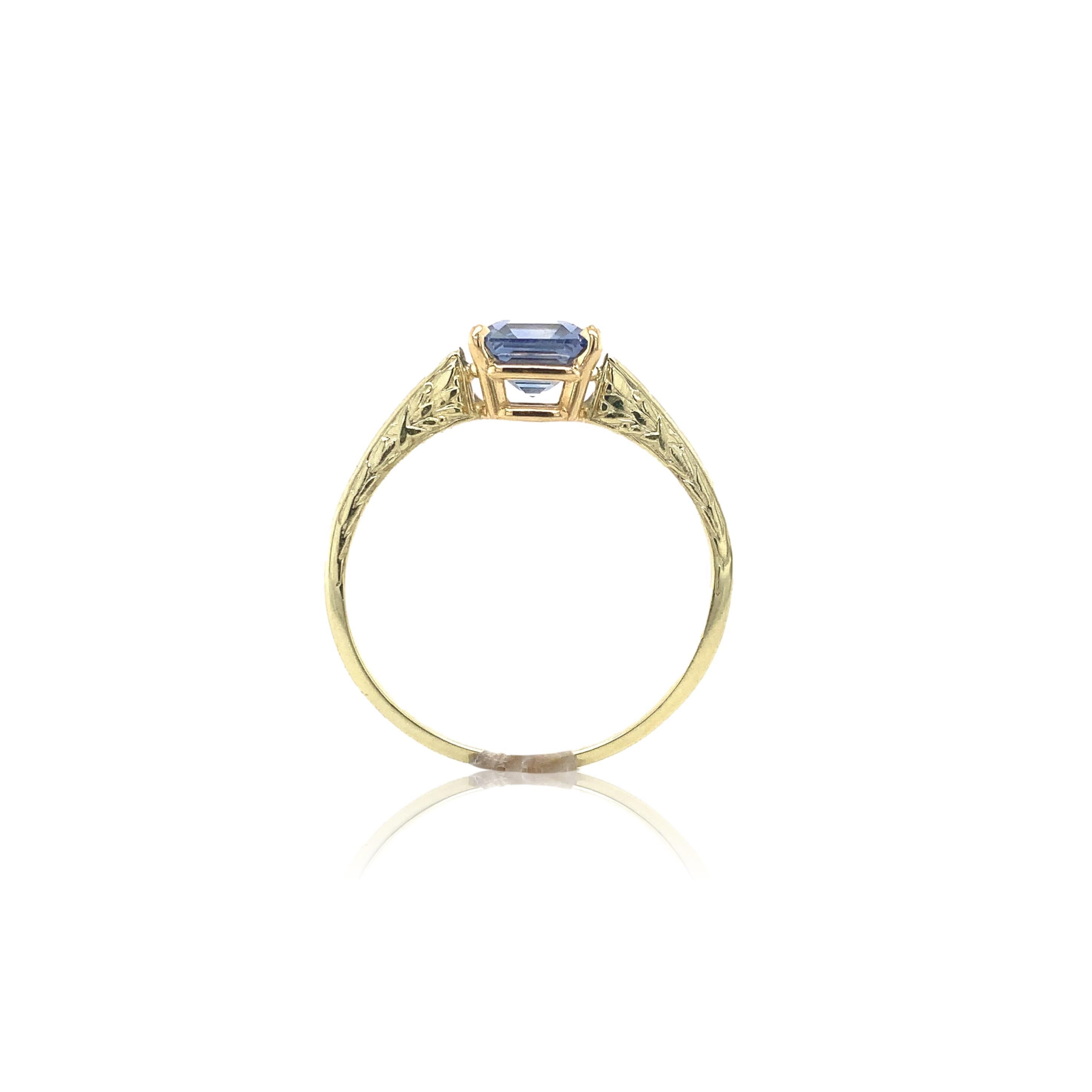 14K yellow gold ring featuring an asscher cut blue Ceylon sapphire weighing 1.44 carats. The sapphire has lavender to periwinkle blue color and measures about 6.5mm. The ring has a leaf design on 2 sides and engraving on the top. There is some wear
