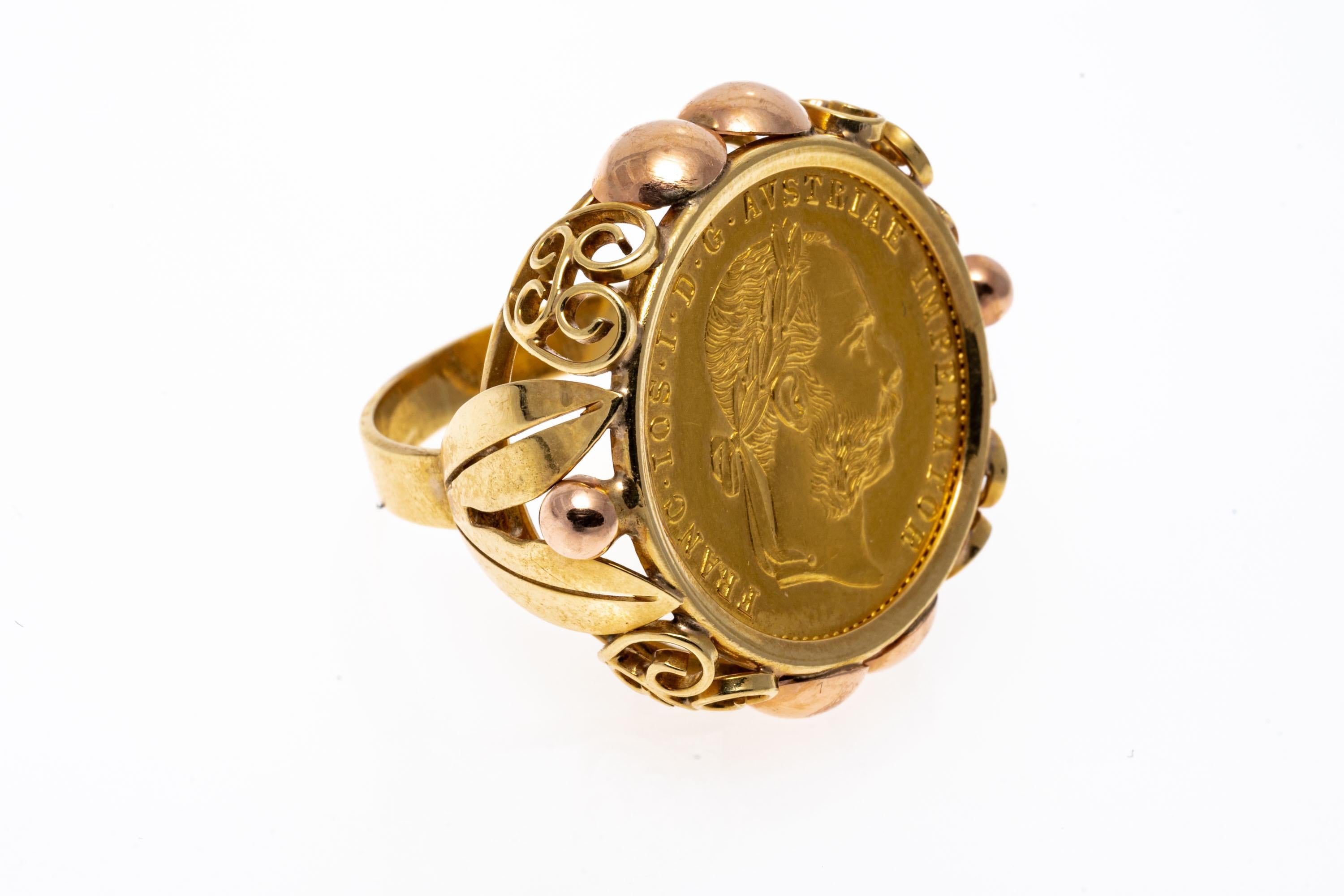 14k yellow gold ring. This elaborate and striking ring contains a center, is a 1915, Austria 4 Ducat coin, set into a yellow gold bezel and decorated with round, rose gold beads and yellow gold scroll patterns on both the frame and the gallery. The
