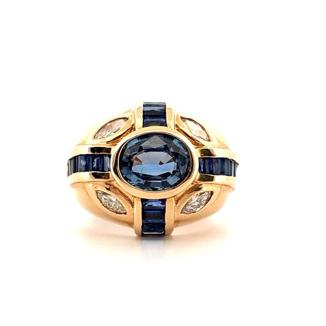 Réalisée en or jaune 14 carats, cette bague vintage audacieuse est ornée en son centre d'un saphir bleu ovale de 2,00 carats, d'une teinte profonde et veloutée. Le saphir est rehaussé par des saphirs baguettes sertis en canal qui courent le long de