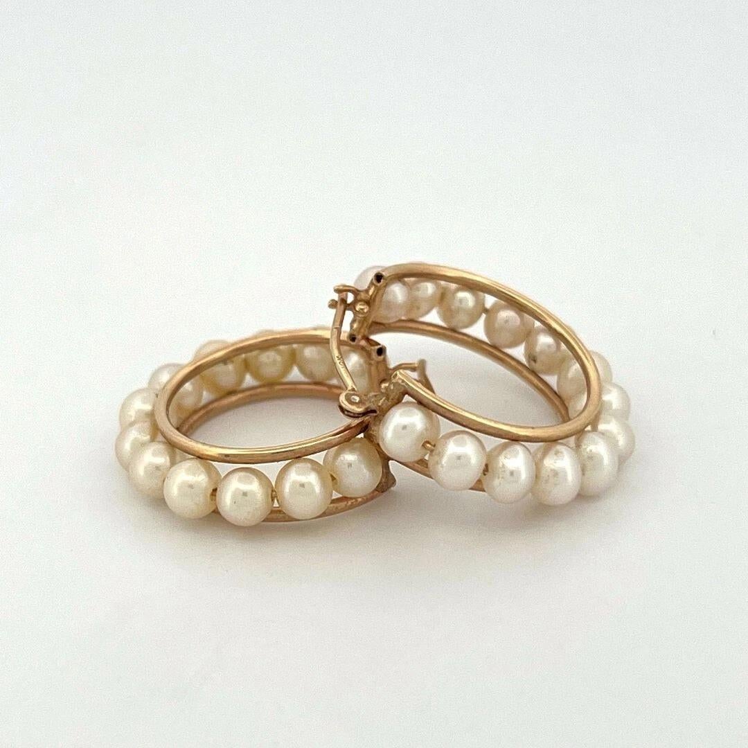 A vintage-inspired pair of elegant 14K yellow gold hoop earrings set with a row of luminous cultured freshwater pearls. Each hoop features pearls measuring approximately 4.0mm, evenly spaced around a 22mm frame, creating a timeless silhouette that’s