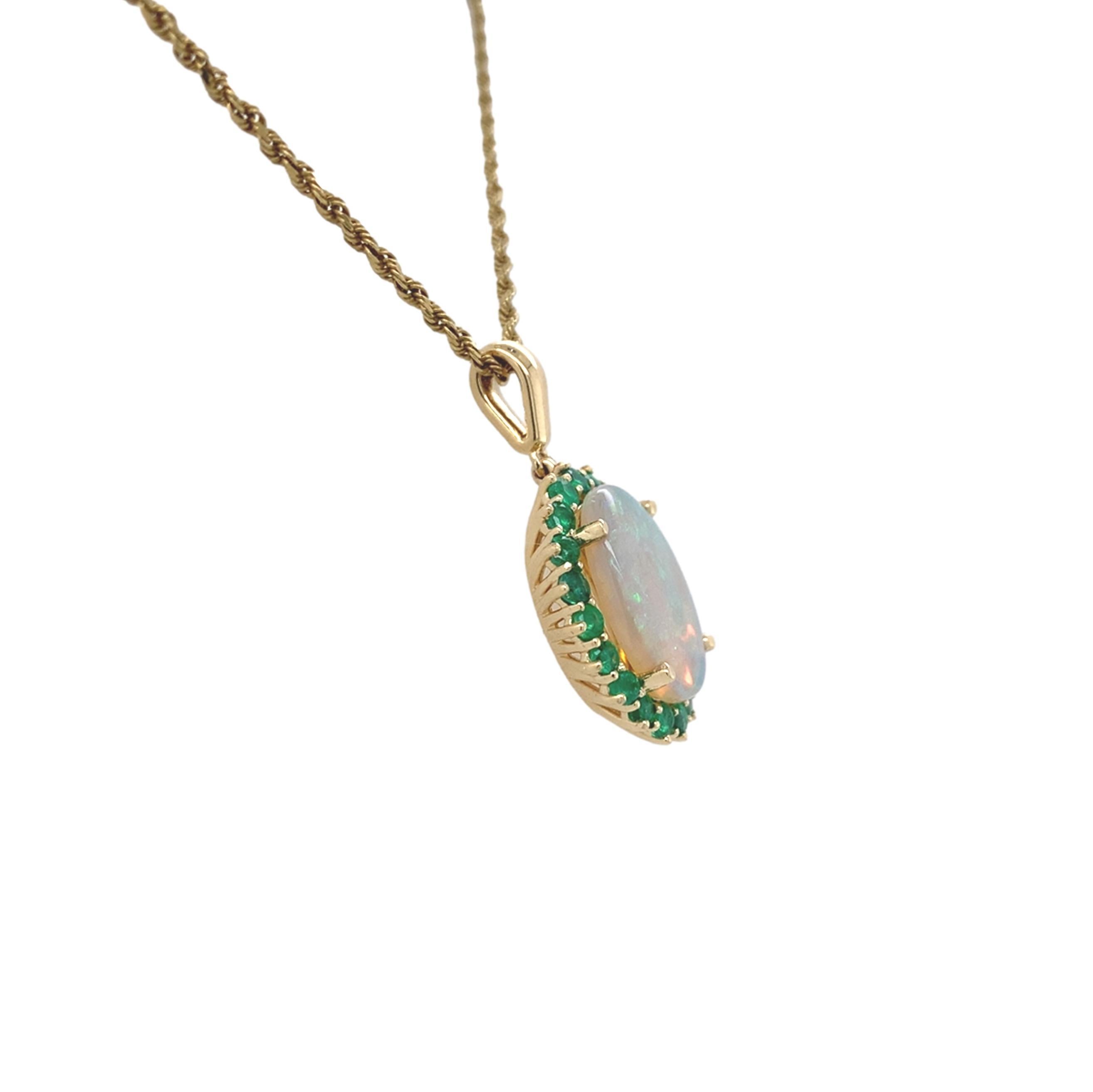 Pendentif en or jaune 14 carats de 2,83 carats en opale australienne avec émeraudes. L'opale ovale en cabochon présente un jeu de couleurs bleu-vert.  L'opale naturelle extraite de la terre mesure environ 14,3 mm x 9,7 mm. Il y a 20 émeraudes rondes