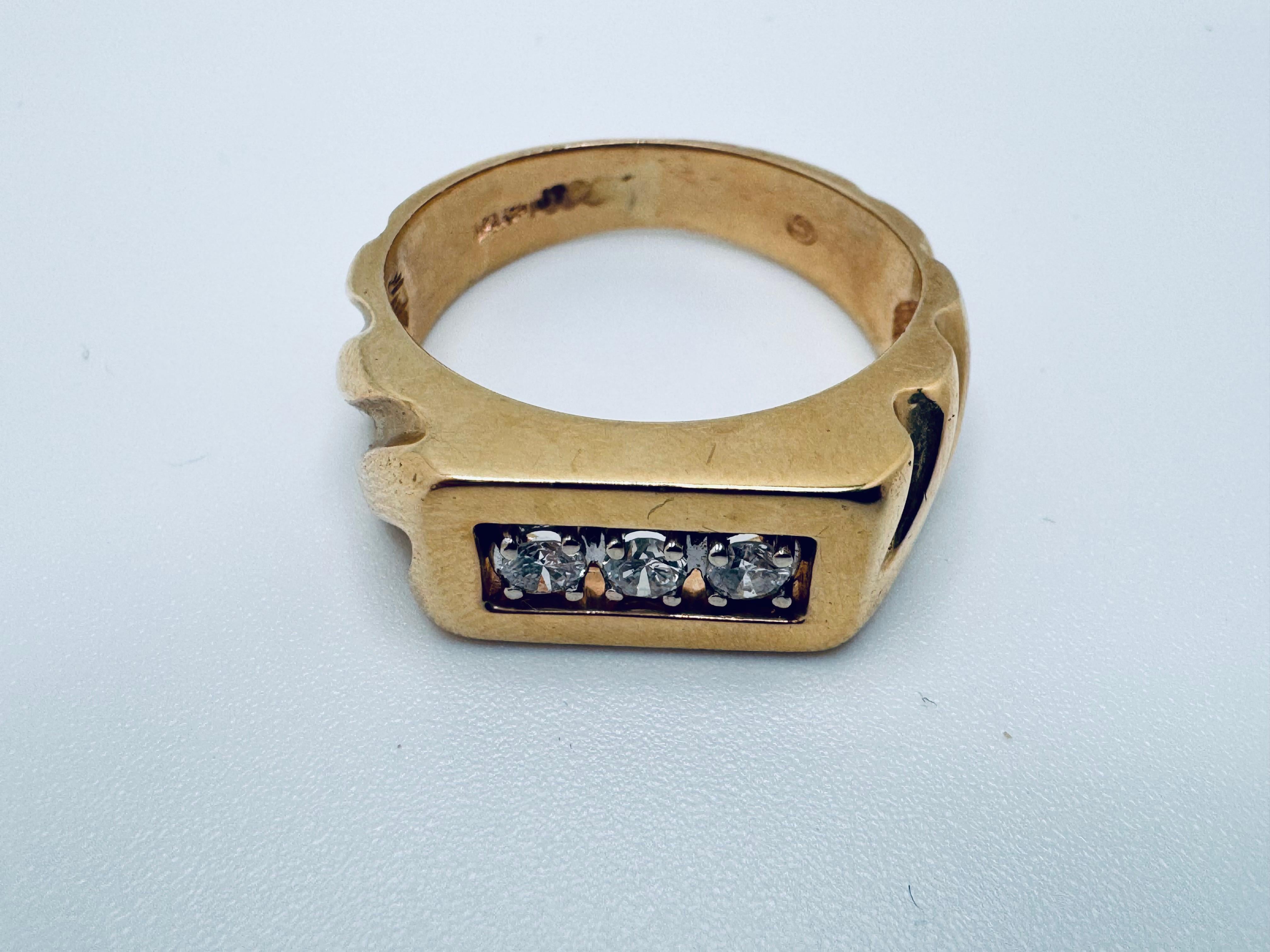 Este anillo para hombre está fabricado en oro amarillo macizo de 14 quilates y presenta un diseño atrevido pero refinado. Engarzados en la parte delantera hay tres diamantes redondos de talla brillante, que ofrecen un peso total en quilates de