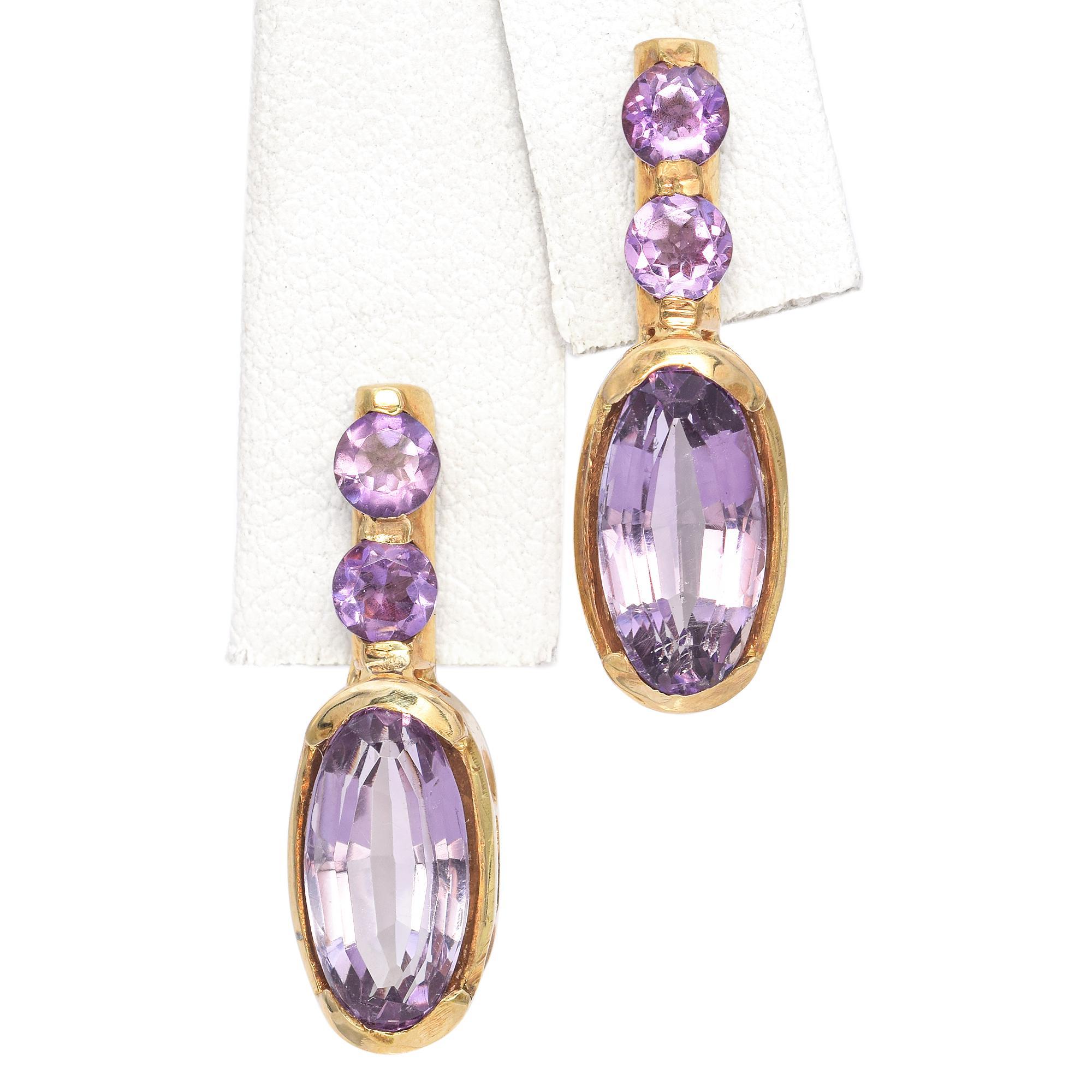 Cette exquise paire de boucles d'oreilles est réalisée en or 14k. Les boucles d'oreilles sont ornées d'améthystes de taille ovale d'une riche teinte violette. Le design met en valeur deux améthystes rondes plus petites au-dessus des pierres plus