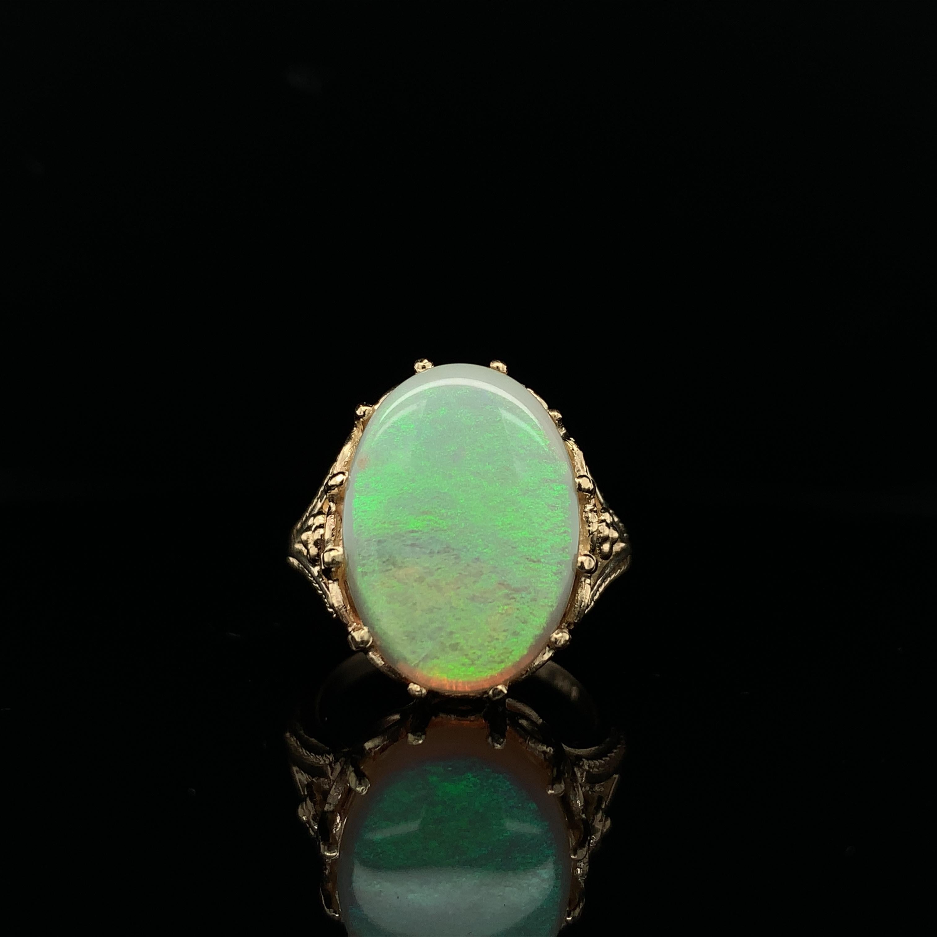 14K yellow gold ring featuring an oval Australian opal weighing 5.86 carats and measuring about 18mm x 12.8mm. The opal has primarily green pin-fire play of color with a little yellow. This opal is freshly polished and has a ton of color. The ring